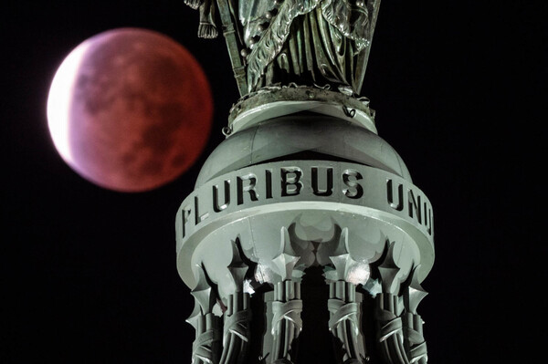 The moon, with a partial lunar eclipse, is seen behind the writing E Pluribus Unum, latin for "Out of many, one" on the Statue of Freedom at the top of the dome on Capitol Hill in Washington, DC on Nov. 19.