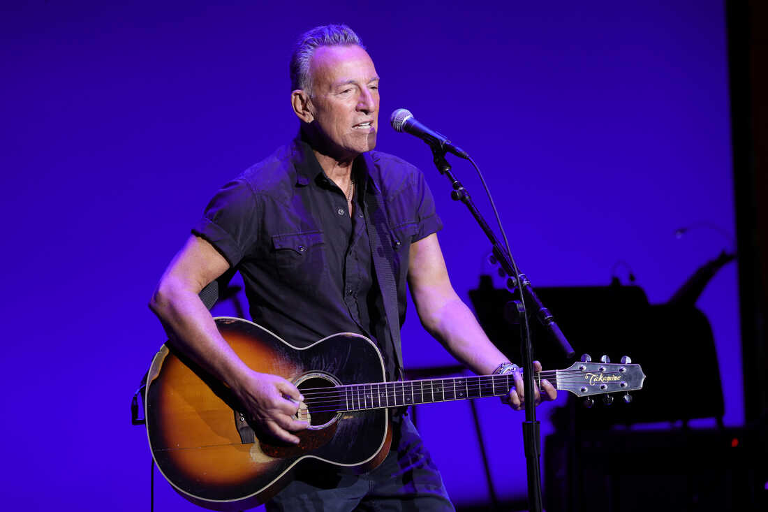 Bruce Springsteen carrying a guitar and singing onstage