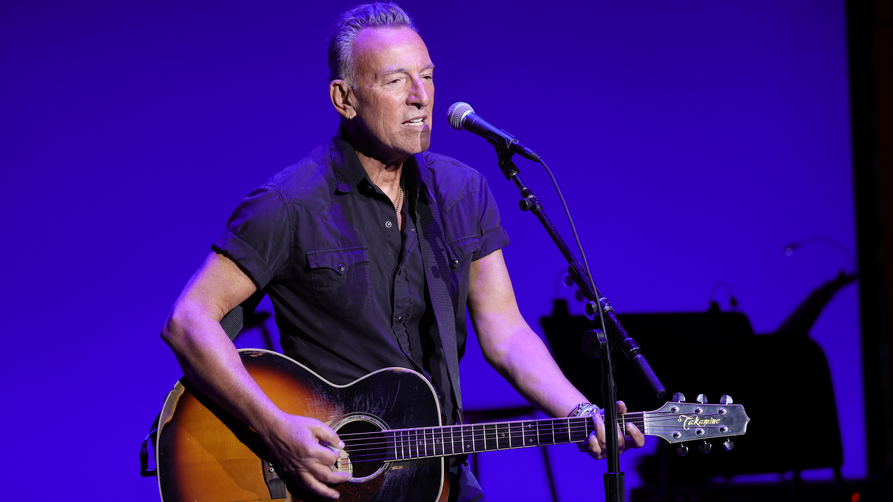 Bruce Springsteen carrying a guitar and singing onstage