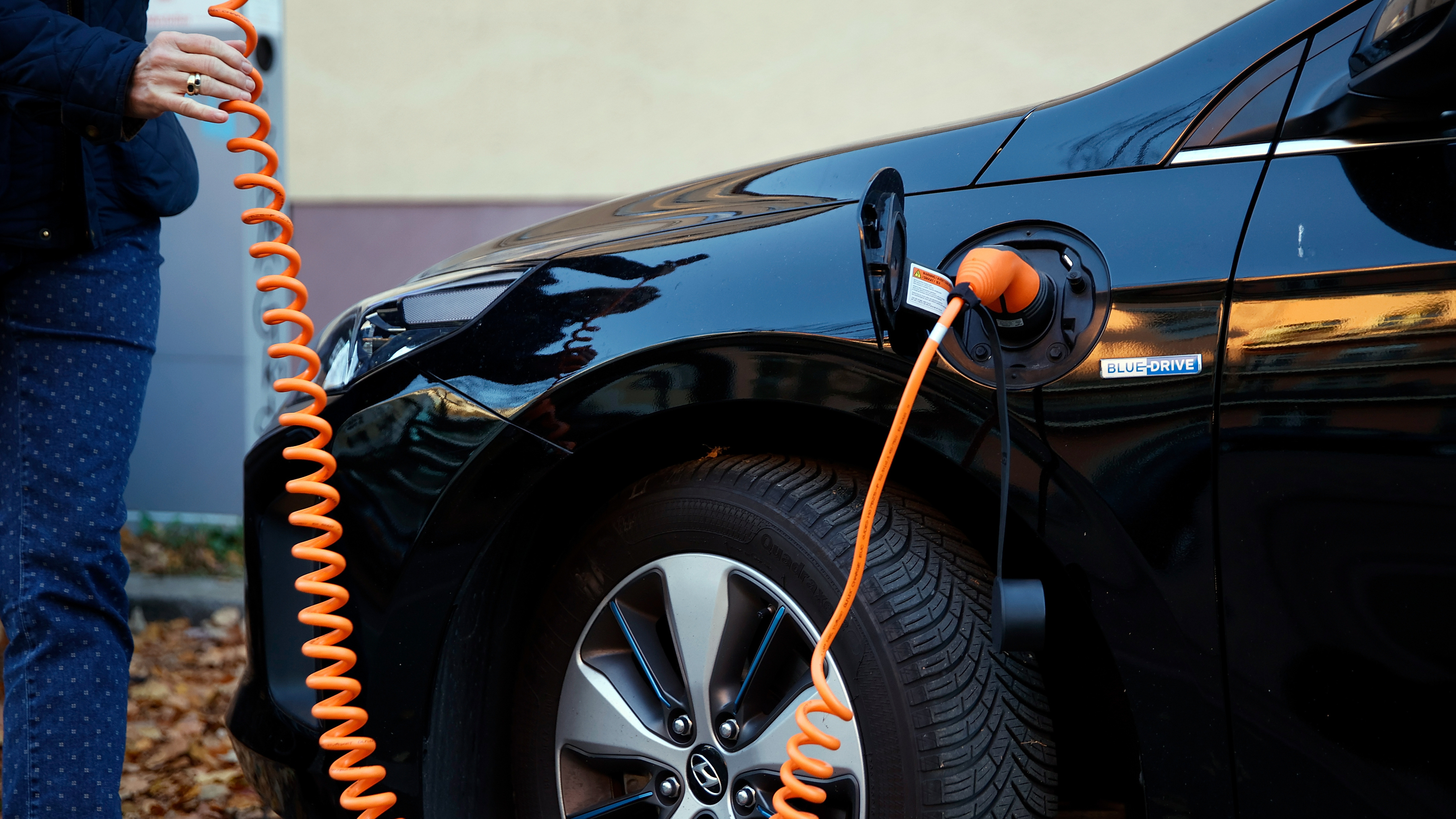 The driver of an electric car handles the charging cable to charge the car at a public charging station in Berlin, Germany. (Getty Images)
