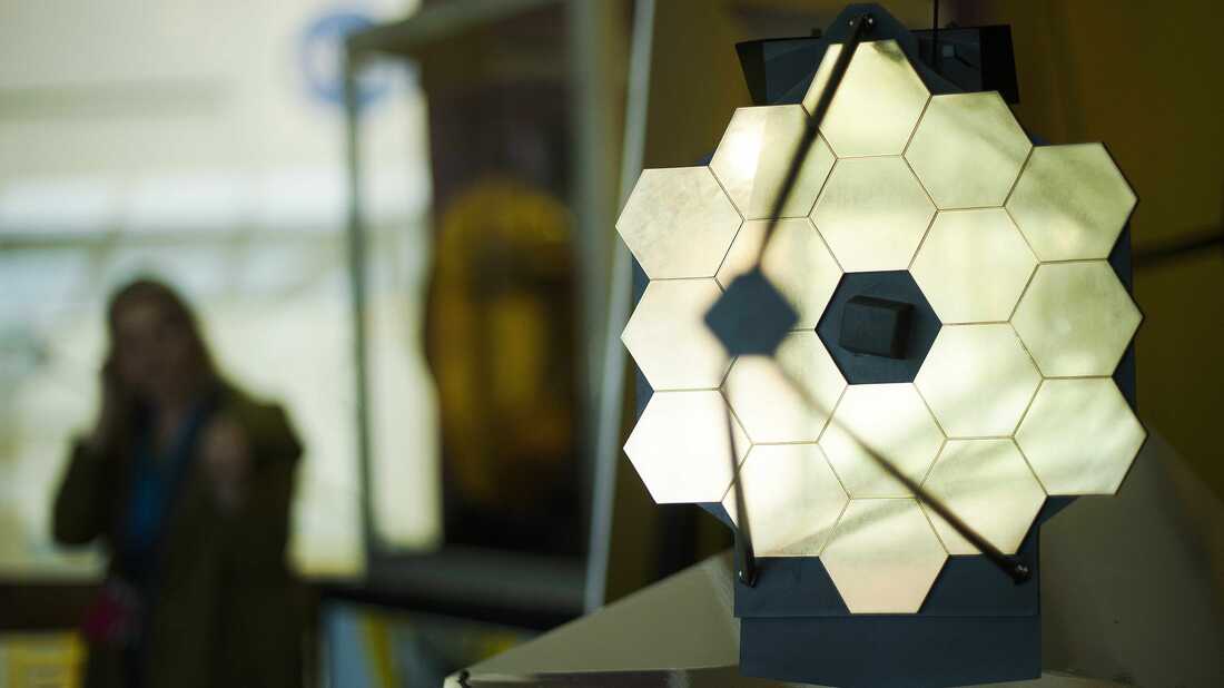 A woman stands near a model of the James Webb Space Telescope (JWST) at NASA Goddard Space Flight Center.