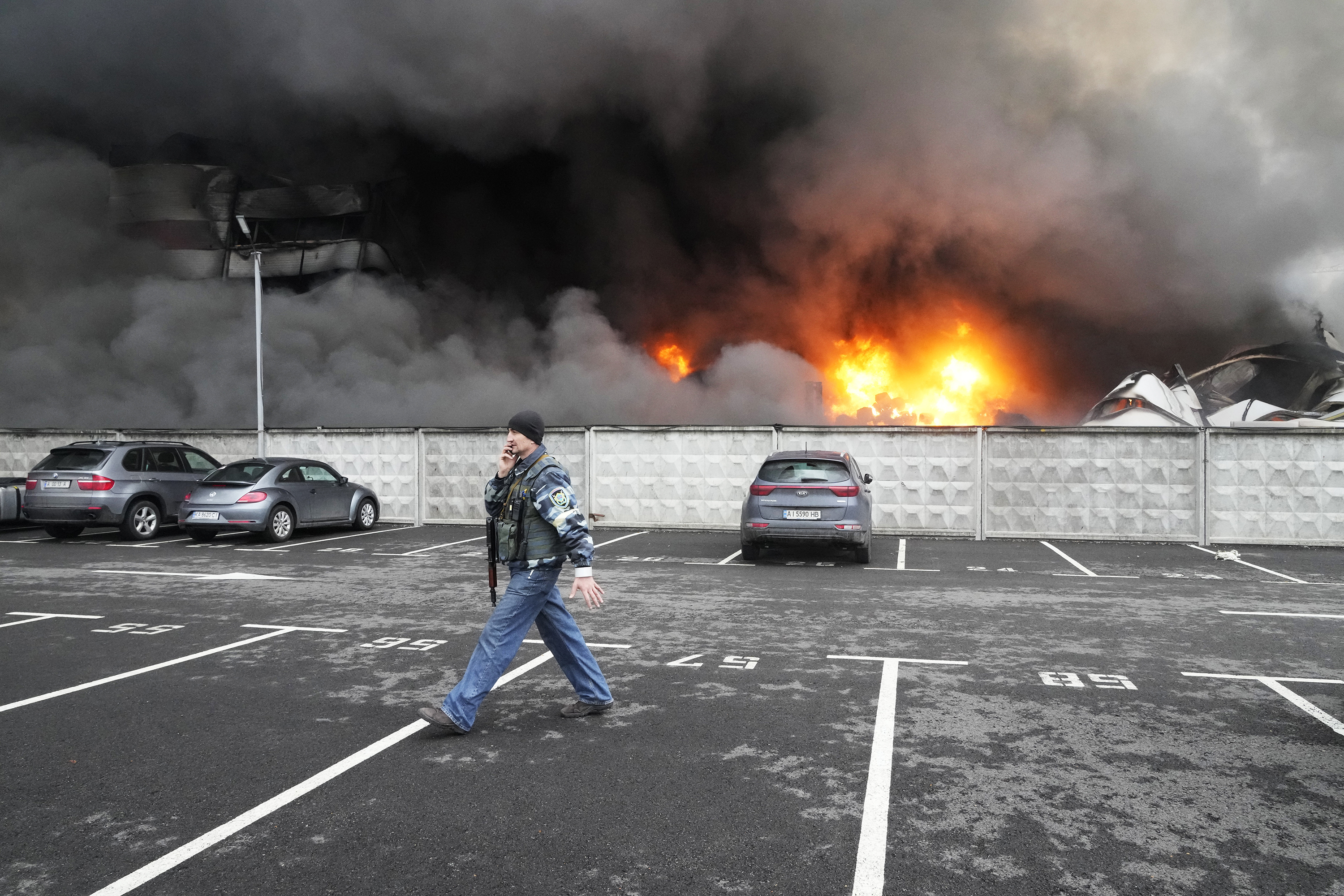 A Ukrainian serviceman walks past as fire and smoke rises over a damaged logistics center after being shelled Thursday, March 3, in Kyiv, Ukraine.