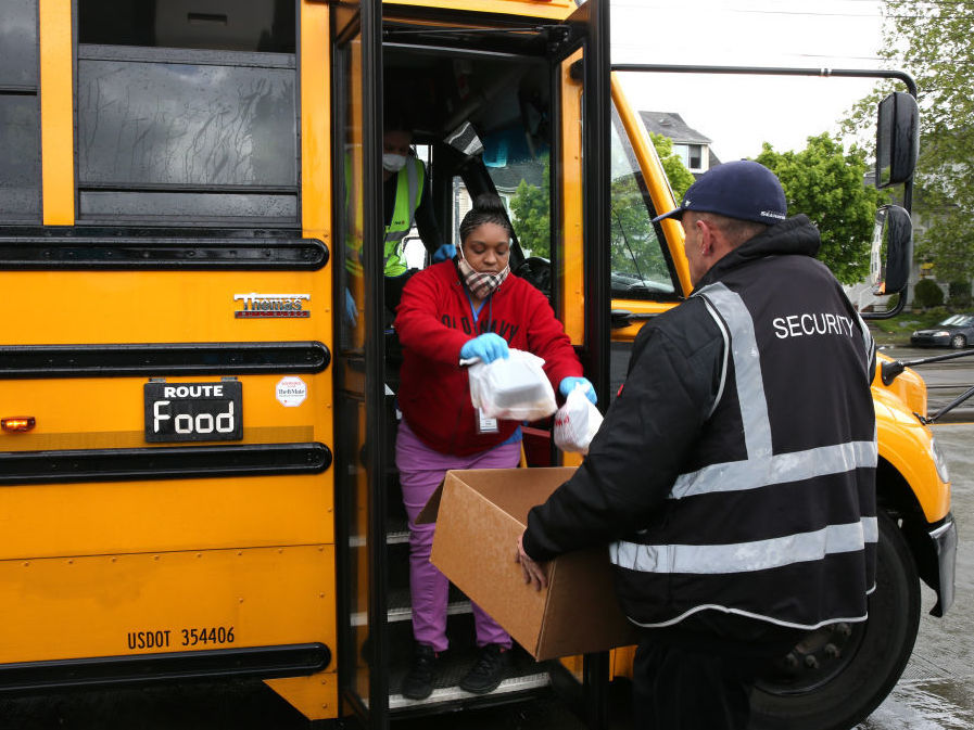 Nutritionist Shaunté Fields (center) and bus driver Treva White (behind Fields, on the bus) deliver meals to children and their families in Seattle. When schools closed because of COVID-19, Seattle Public Schools began distributing breakfast and lunch to students through a network of 26 school sites and 43 bus routes five days a week. (Getty Images)