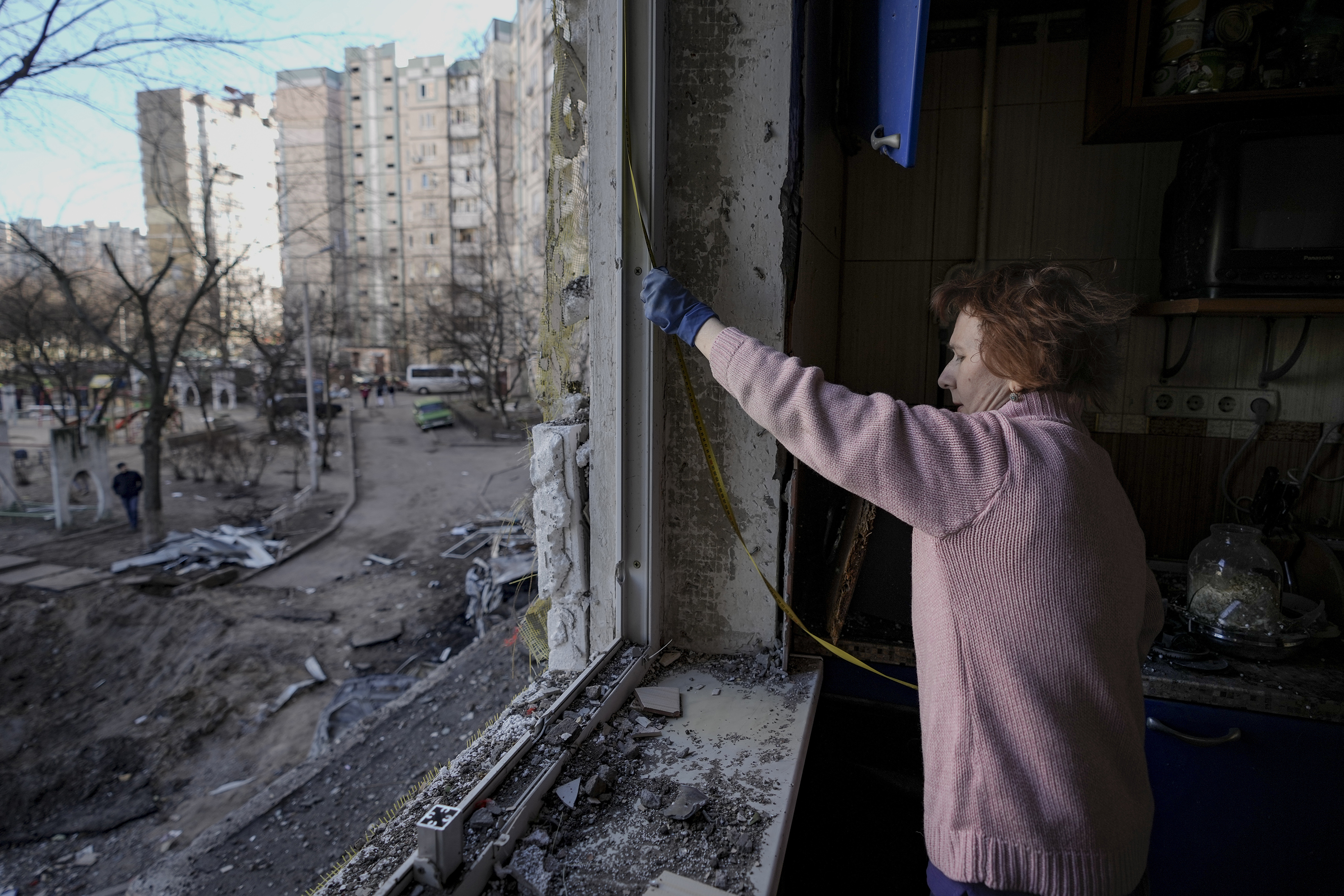 March 21: A woman measures a window before covering it with plastic sheets in a building damaged by bombing Sunday in Kyiv.