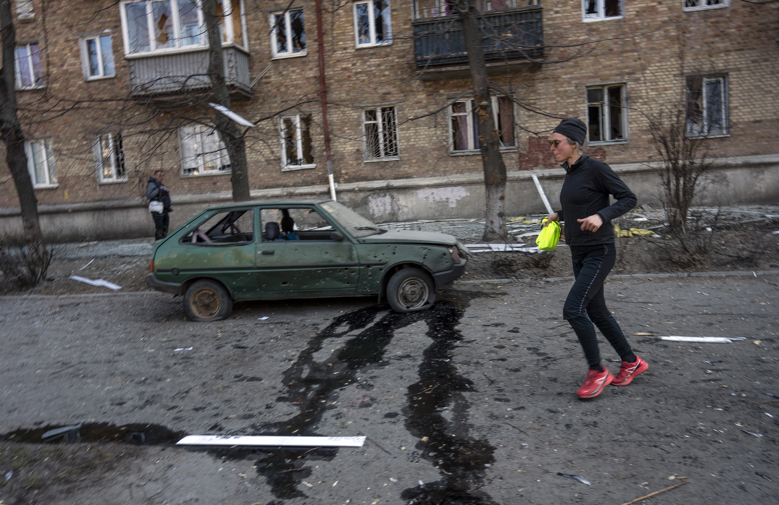 March 23: A woman exercises near a car and apartments damaged by shelling in Kyiv.