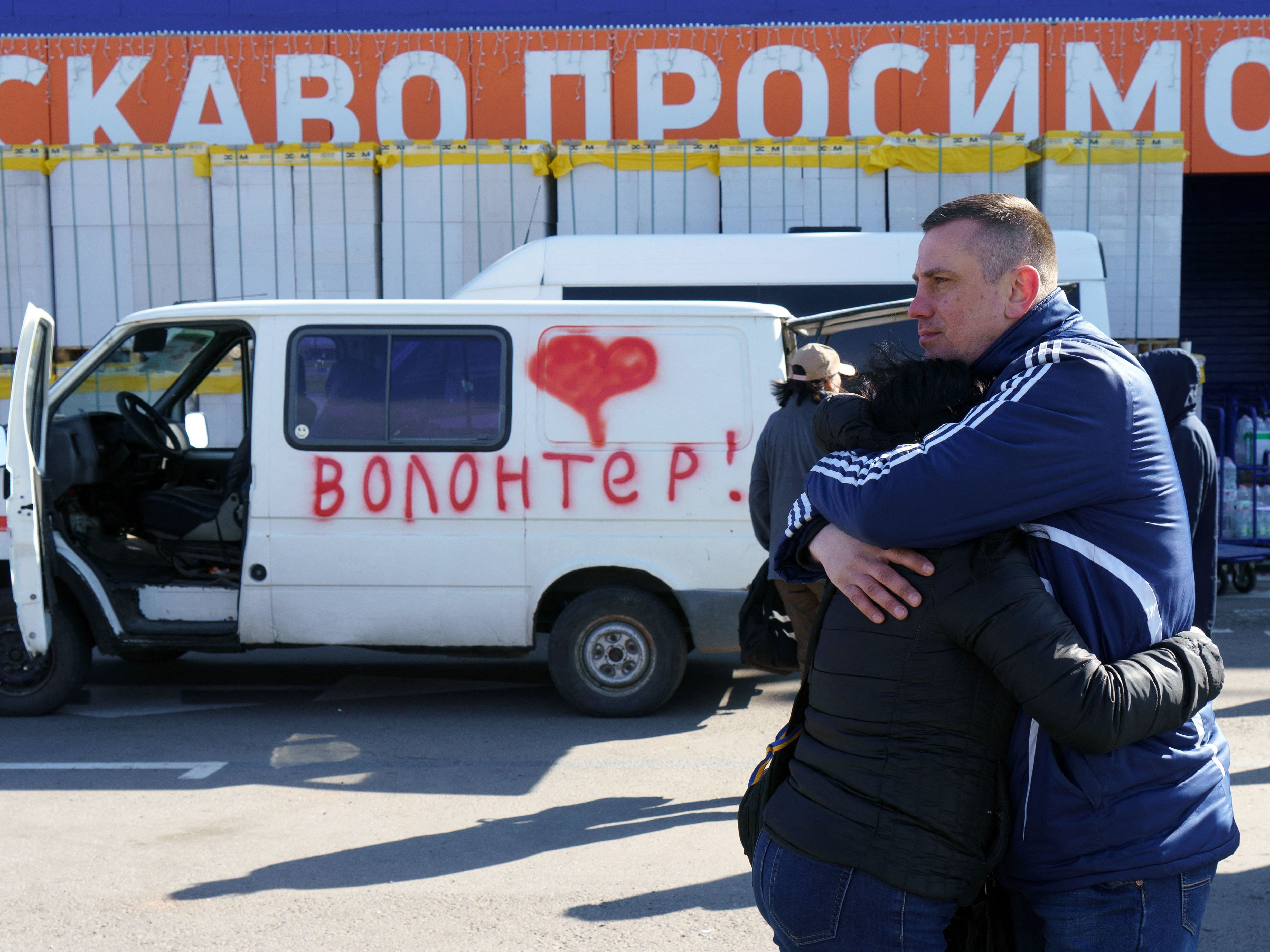 Olga and Oleksandr hug as they wait beside a vehicle painted with the word &quot;volunteers&quot; at an evacuation center in Zaporizhzhya, Ukraine, on Tuesday. Olga's father is stuck in Mariupol, and Oleksandr is hoping to get in a volunteer convoy to the city, now under Russian siege. (AFP via Getty Images)