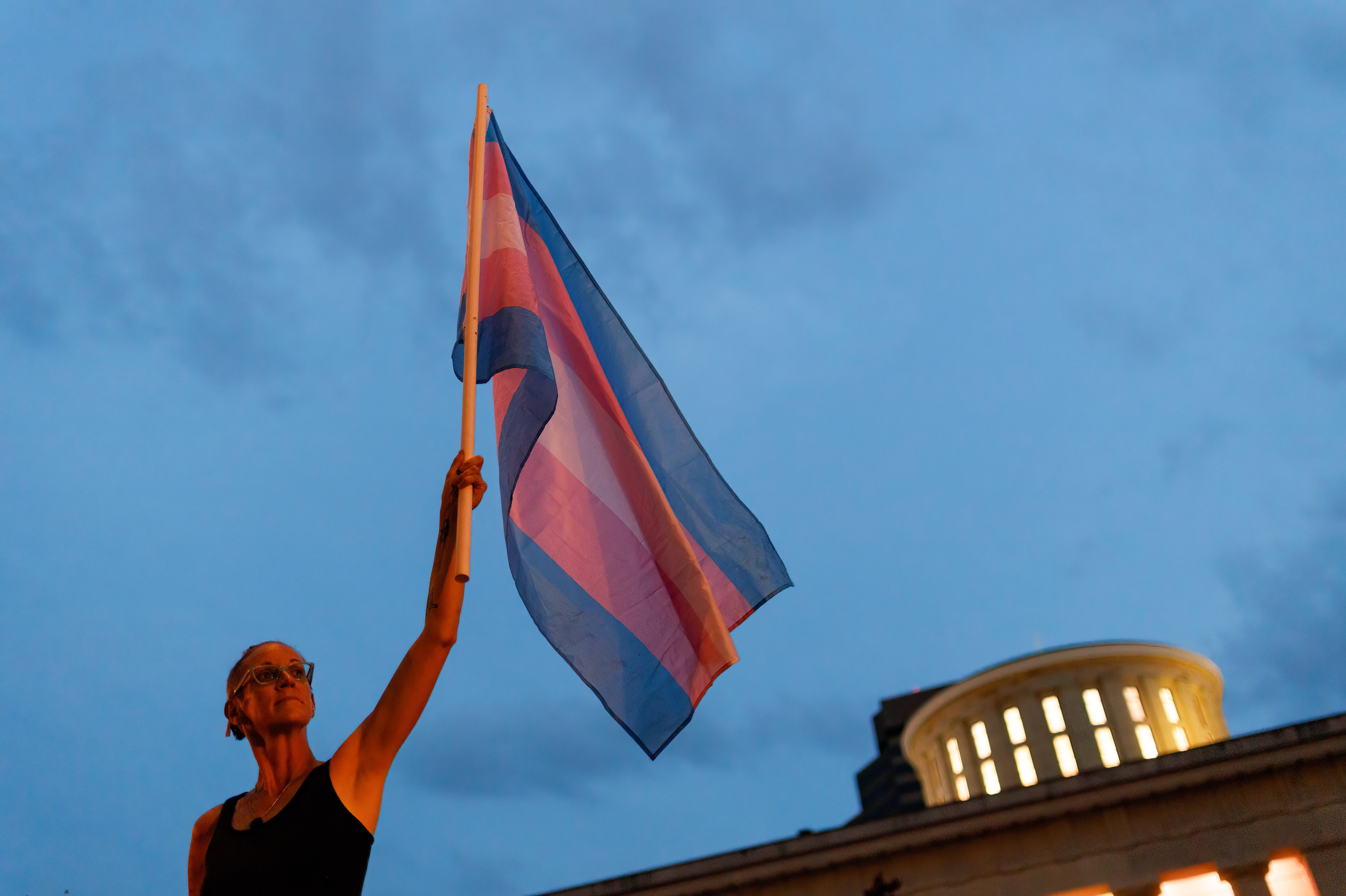 Cole Ramsey, 39, of South Linden, Ohio, holds a Transgender Pride Flag in front of the Ohio Statehouse in Columbus to protest the passing of legislation against trans women playing sports in high school and college. (SOPA Images/LightRocket via Getty Images)