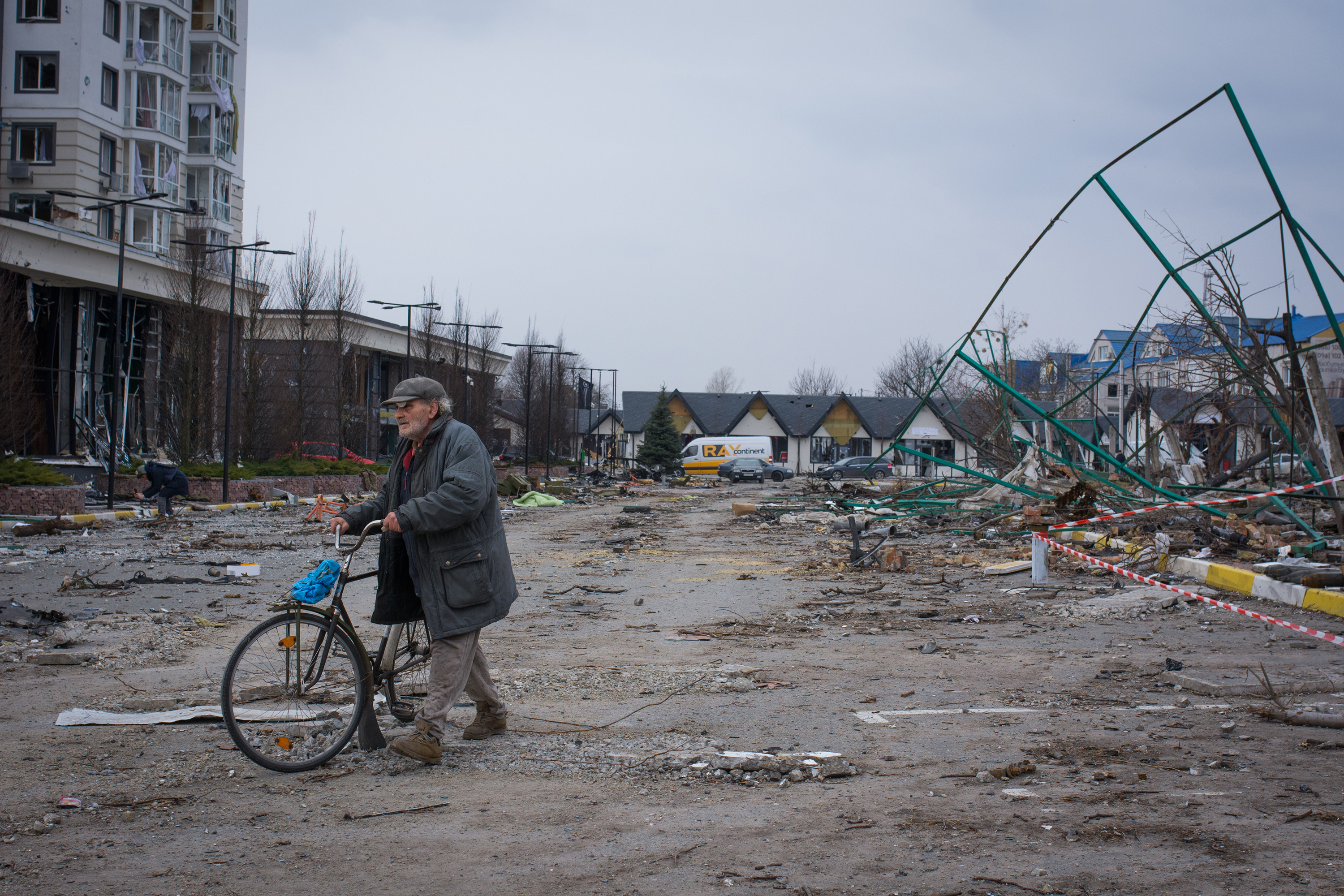 A man walks his bike through a parking lot littered with broken glass in Bucha, Ukraine. (NPR)