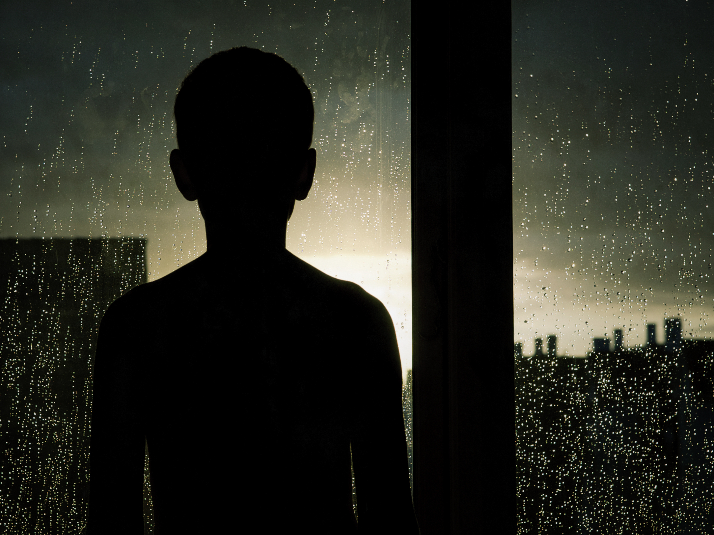 A child looking out the window on a rainy day.