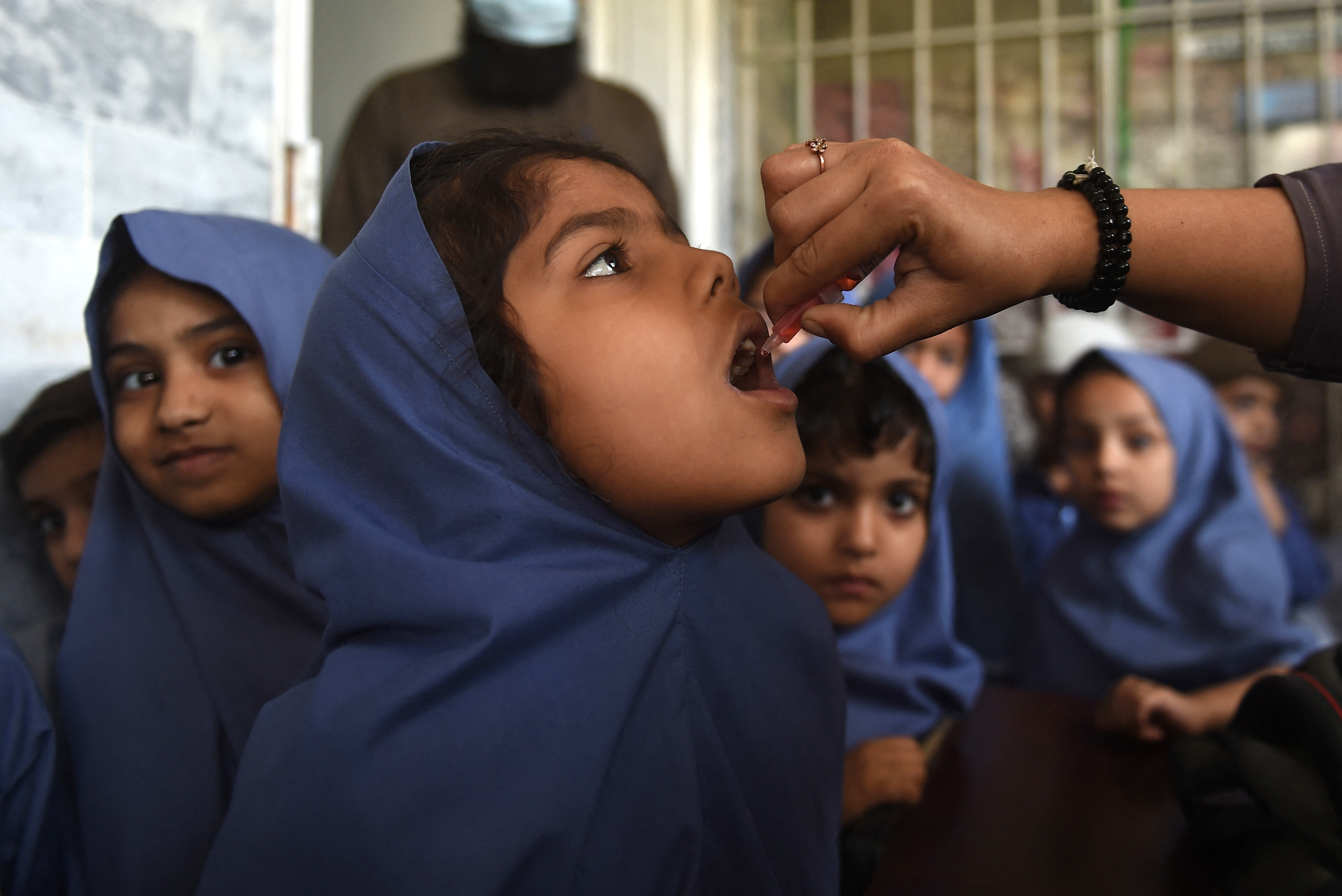 A health worker administers the oral polio vaccine to a young girl as other children wait for their turn at a school in Karachi, Pakistan on February 28, 2022. In response to an uptick in cases of vaccine-derived polio — a form of the disease that stems from the oral vaccine — many countries are rolling out a new oral polio vaccine. (AFP via Getty Images)