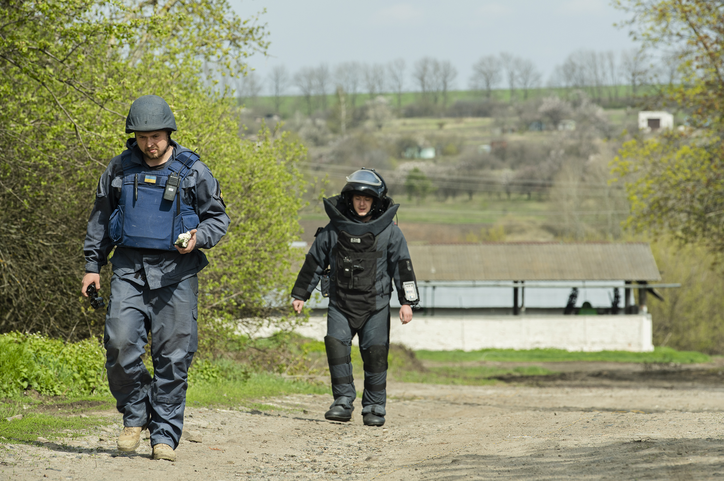 Kharkiv Explosive Ordinance Disposal (EOD) technicians Maksim and Maksim walk back to their truck after detonating the first of 24 unexploded, timed mines. They were able to safely dispose of the mines in Bilashi on Saturday. Maksim (left) is holding the remains of the exploded cluster munition is his left hand. The mine was dropped by a cluster bomb Friday night. (NPR)