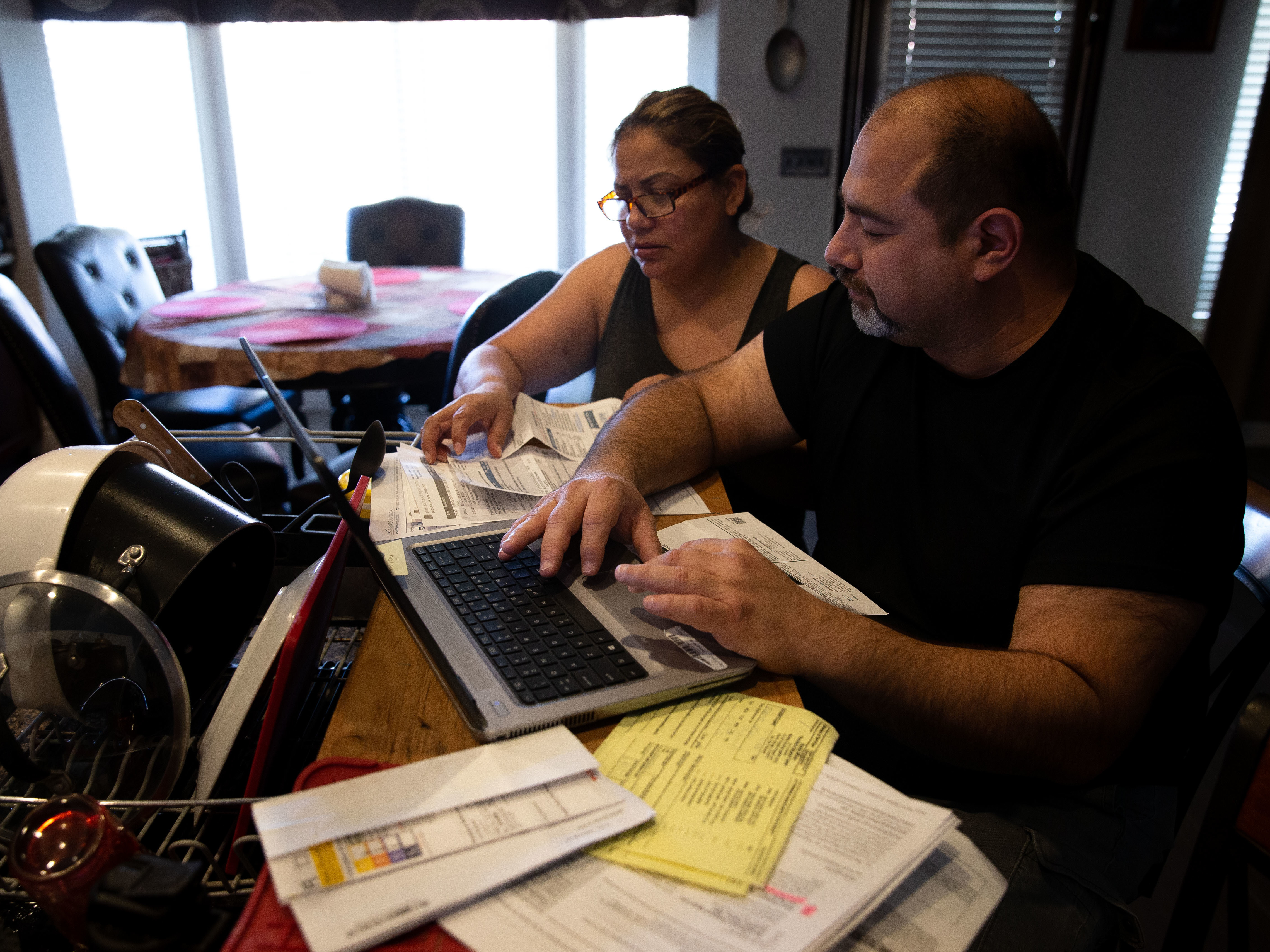 Claudia and Jesús Fierro of Yuma, Ariz., review their medical bills. They pay $1,000 a month for health insurance yet still owed more than $7,000 after two episodes of care at the local hospital. (Lisa Hornak for Kaiser Health News)