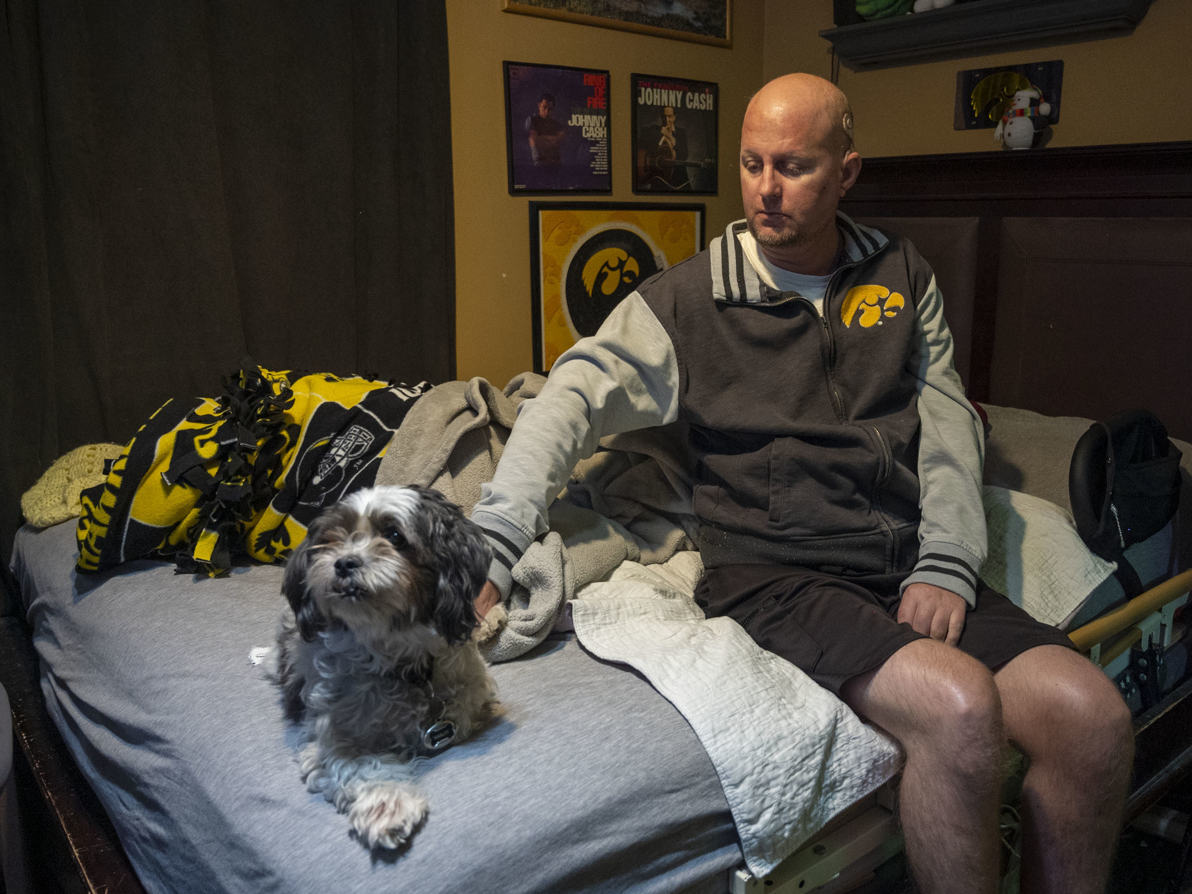 Jon Miller sits in his bedroom with his dog, Carlos, whom he received as a present for successfully completing cancer treatment a decade ago. Miller sustained severe brain damage, and requires the help of home health aides to continue living in his home. (Side Effects Public Media)