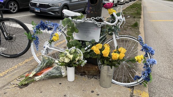 A bike covered in blue and yellow flowers is chained to a pole on the sidewalk.