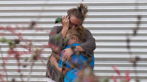 A woman cries and hugs a young girl while on the phone outside the Willie de Leon Civic Center where grief counseling will be offered in Uvalde, Texas.