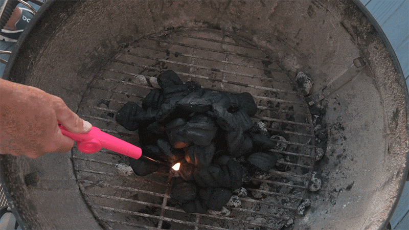 gif of a hand lighting a charcoal grill with a stick lighter 