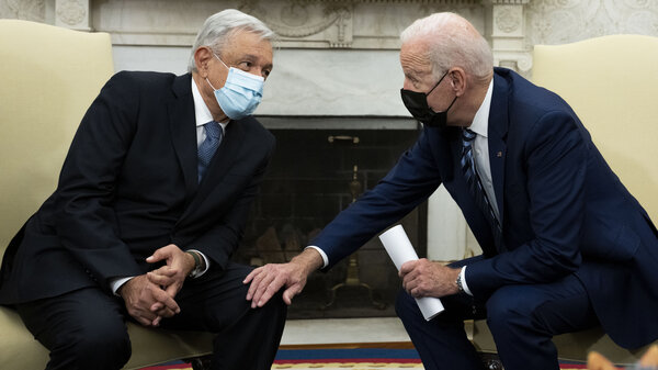 President Biden and Mexican President Andrés Manuel López Obrador, wearing suits and face masks, lean in to speak while seated next to each other.