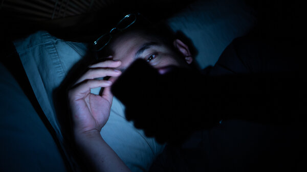A man lays in bed in the dark looking at his phone