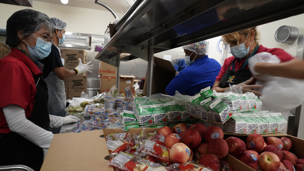 Los Angeles Unified School District food service workers pre-package hundreds of free school lunches in plastic bags.