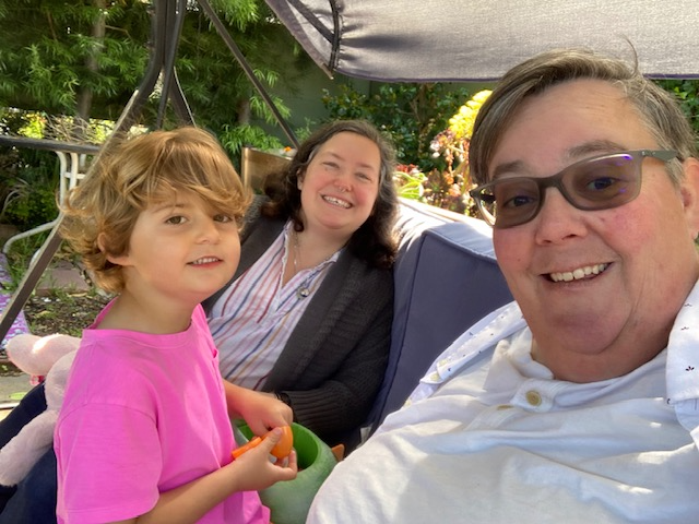A selfie of Beth Kenny (foreground), their wife Adina (middle), and their child Vyla sitting in their backyard in Alameda, Calif. Since the lifting of COVID safety measures, Kenny and their family have had to pull back from indoor activities, and they struggle to explain why to Vyla. (Beth Kenny)
