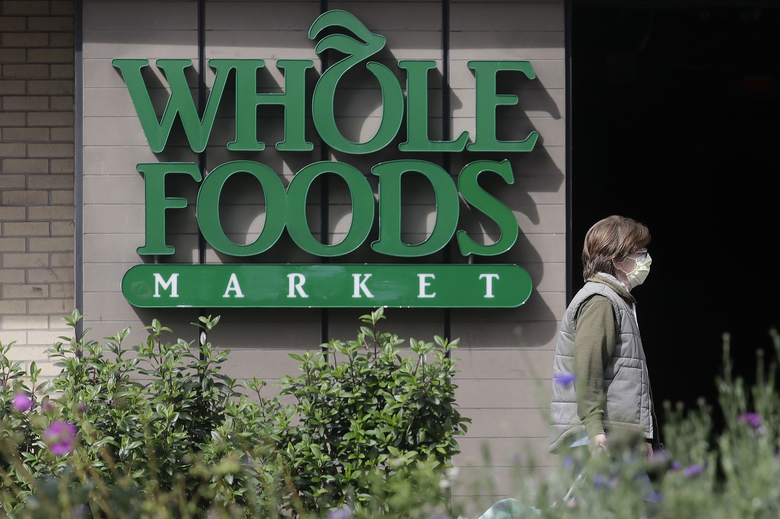 A pedestrian wears a mask while walking past a sign for a Whole Foods Market in San Francisco, Tuesday, March 31, 2020.