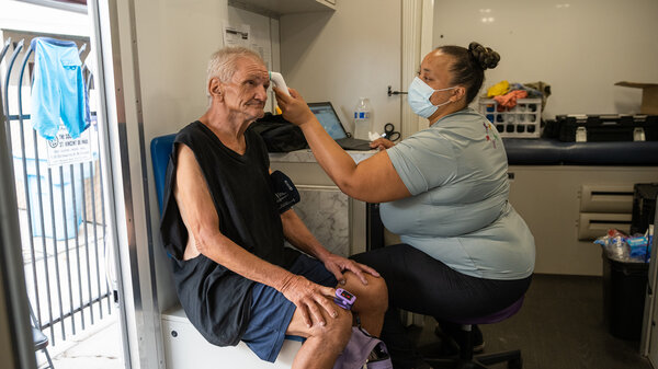 Alicia Williams checks the vital signs of Paul Yager inside the mobile medical unit parked outside St. Vincent de Paul, a charitable organization with a soup kitchen in Phoenix's Sunnyslope neighborhood, on Aug. 9. Yager, 64, is unsheltered, lives with preexisting conditions and has been waiting for housing assistance for two years.