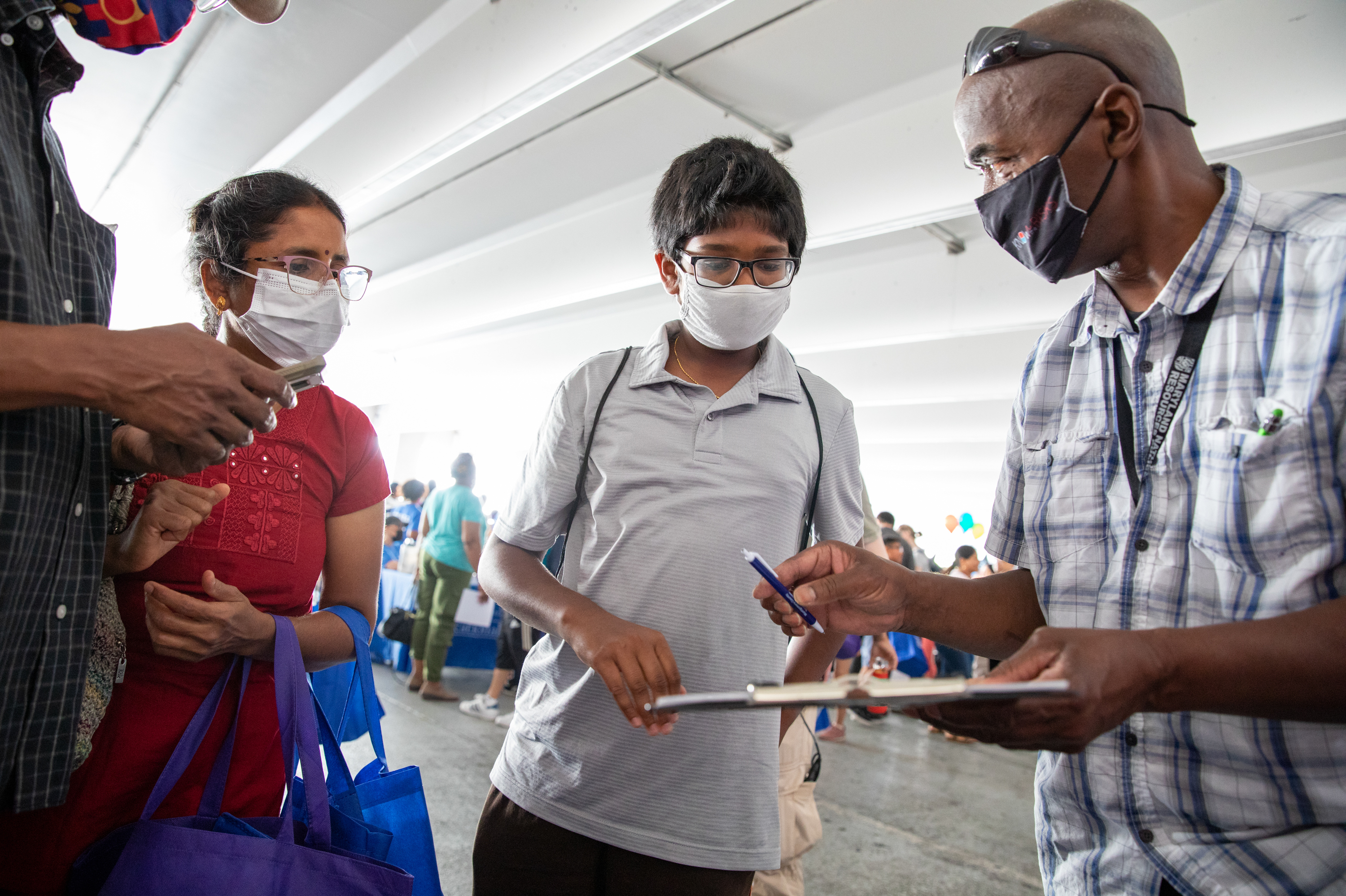 Suseela Kandasamy, left, watches Montgomery County Board of Elections official Ruel Michelin hand her 13-year-old son, Aadhavan Muralidharan, an application to be a student aide to poll workers in Wheaton, Md. (Amanda Andrade-Rhoades for NPR)