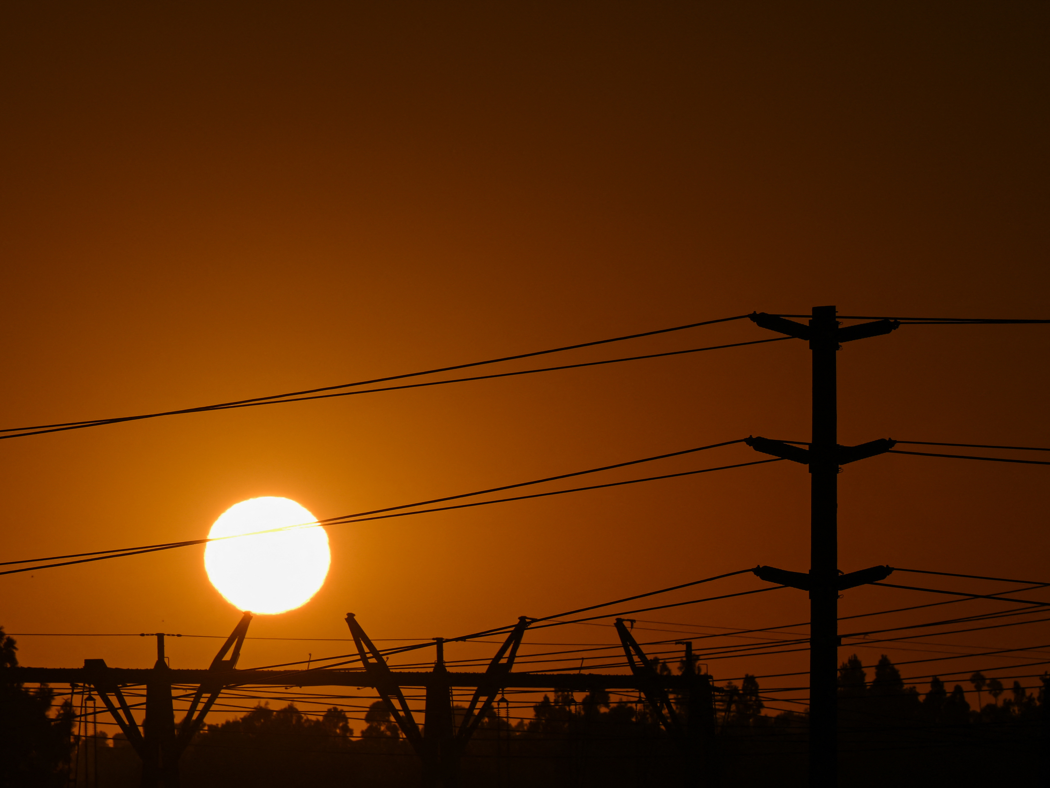 A spike in natural gas prices amid a hot summer is contributing to high electricity bills across the United States. Here, the sun sets behind electric power lines in Redondo Beach, Calif., on Aug. 31. (AFP via Getty Images)