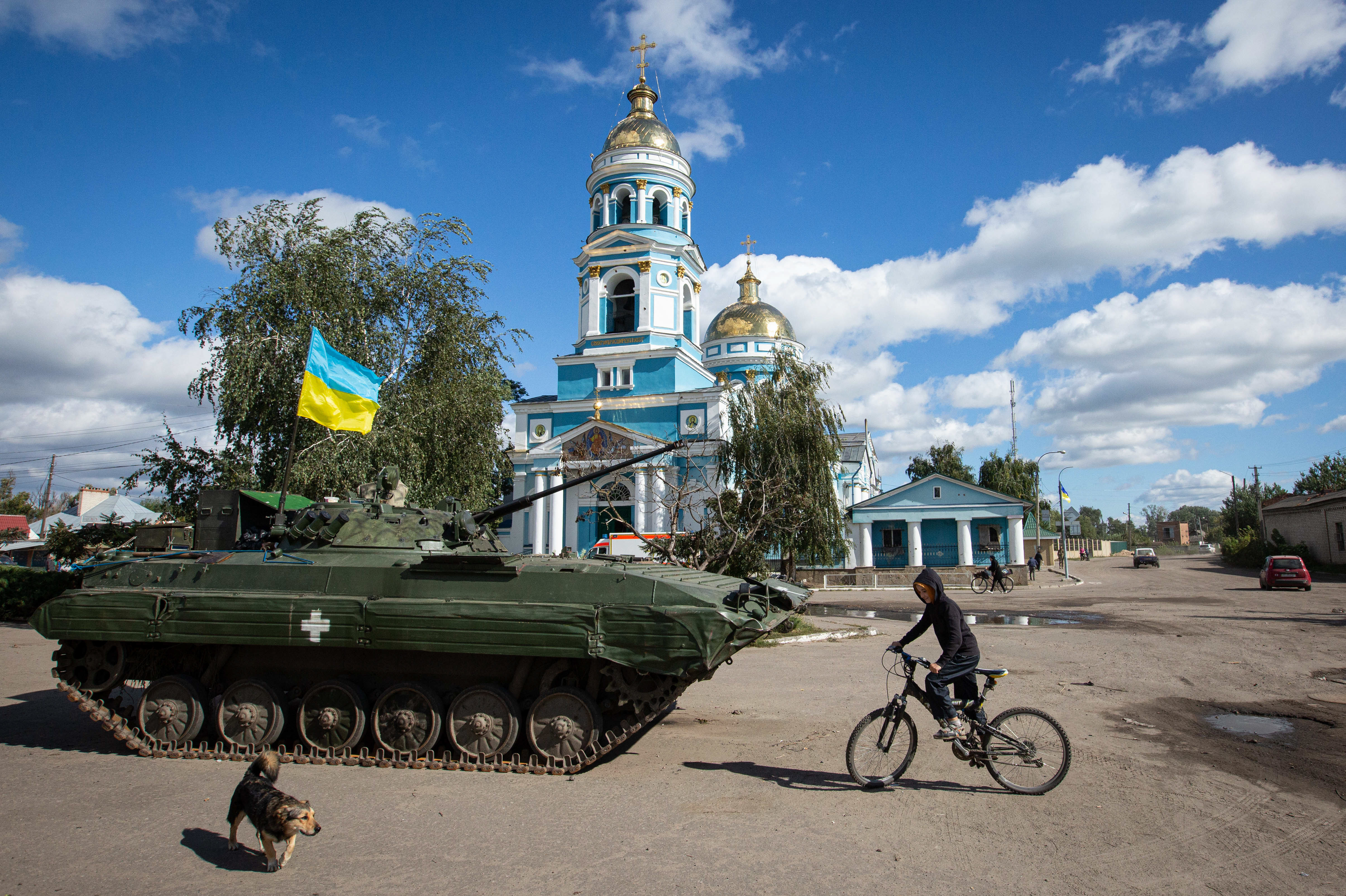 A boy rides a bicycle near an armored tank with a Ukrainian flag in the town of Izium, recently liberated by Ukrainian armed forces, in the Kharkiv region on Monday. Russian troops occupied Izium on April 1. (SOPA Images/LightRocket via Getty Images)