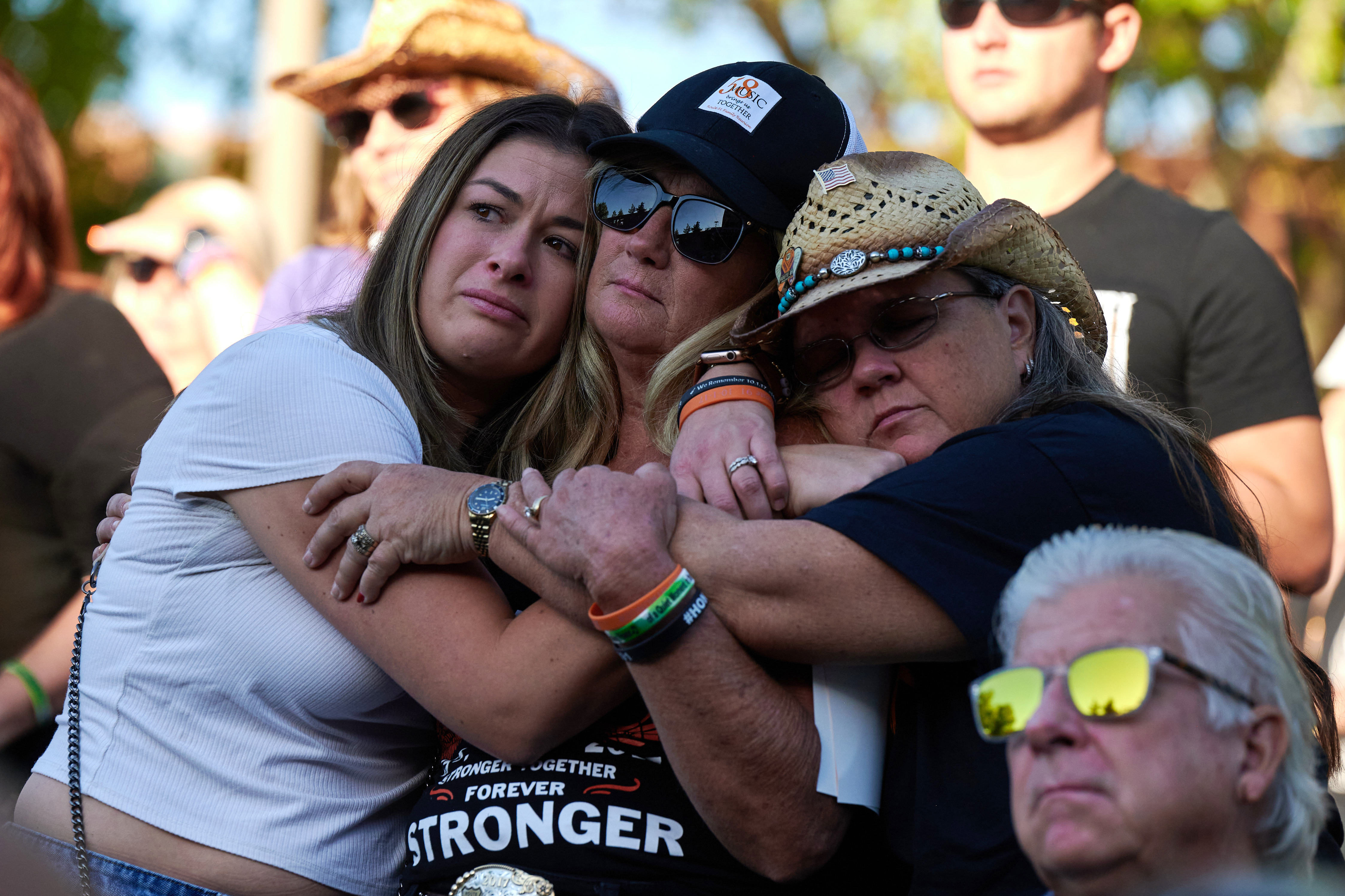 Lauren Reh, Alicia Mierke and Sue Ann Cornwell embrace during the Sunrise Remembrance ceremony at Clark County Government Center Amphitheater in Las Vegas on Oct. 1, 2022. (Bridget Bennett for NPR)