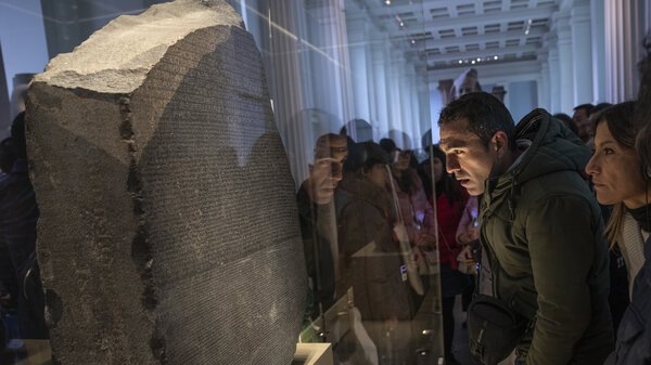 A. man looks at the Rosetta Stone behind glass