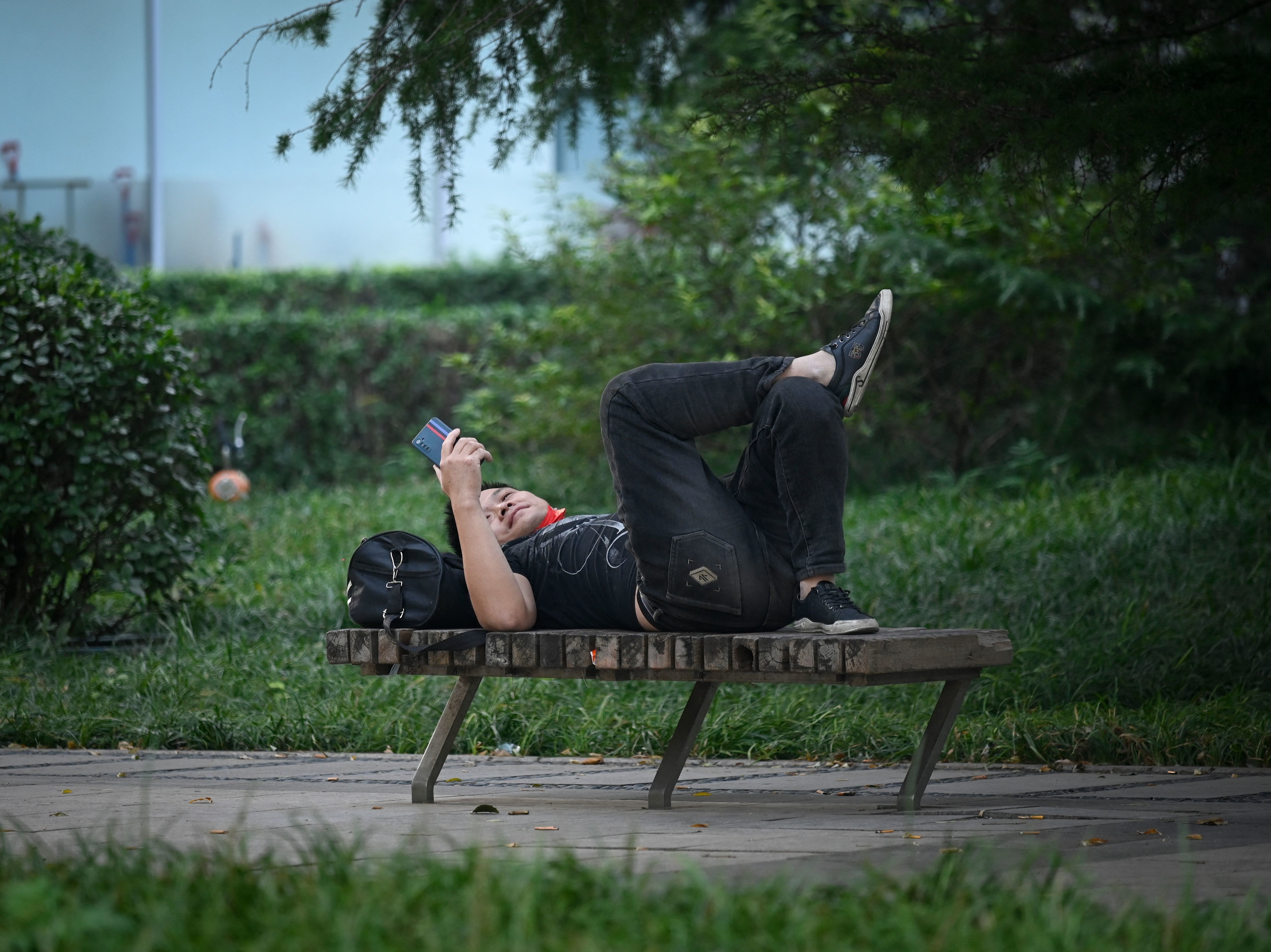 A man uses his mobile phone as he rests on a bench at a garden in Beijing on September 26, 2022. (AFP via Getty Images)