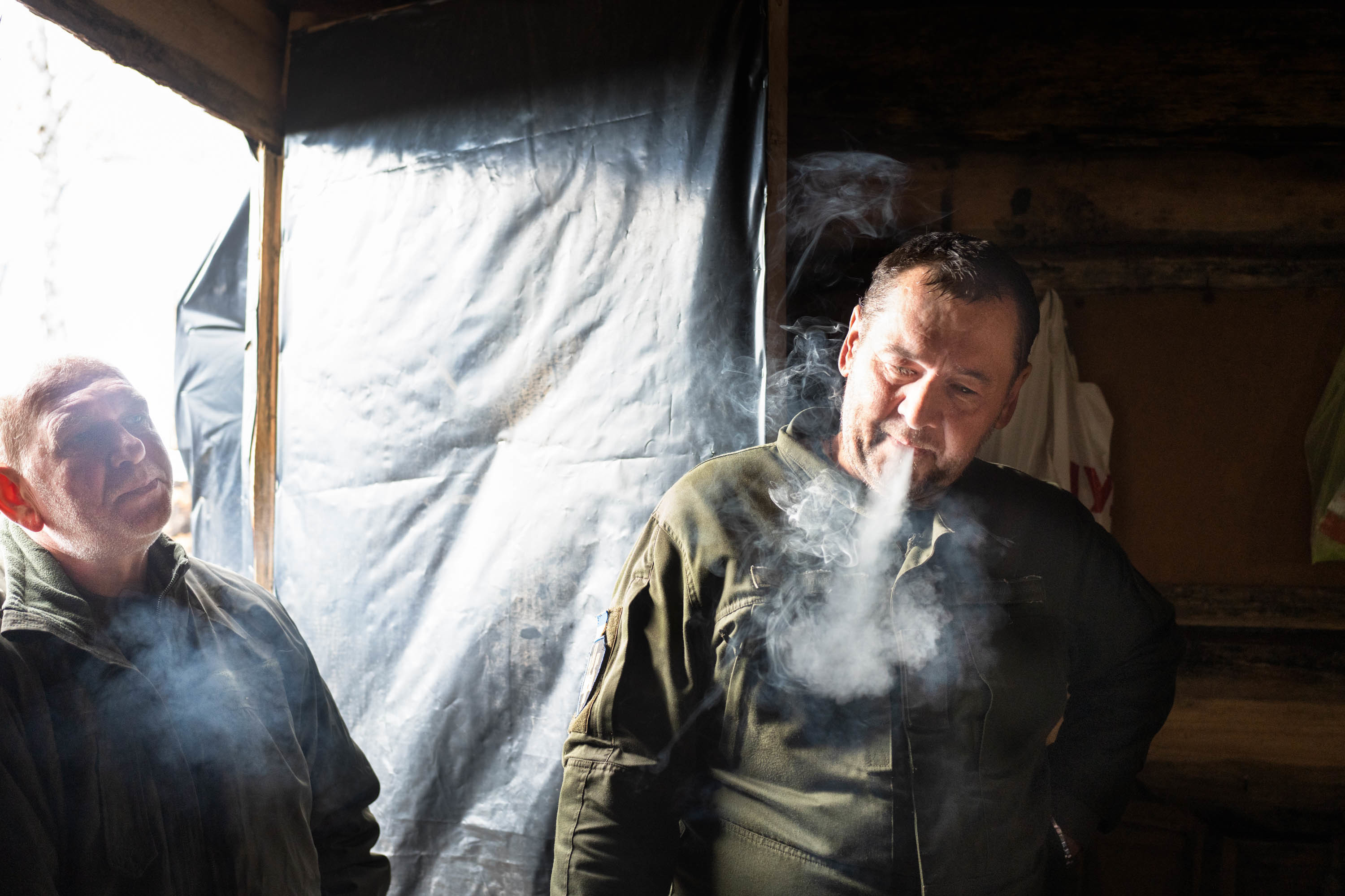 With winter approaching, Ukraine prepares to fight on frozen ground 6 Soldiers smoke near an open door in a building heated by a wood stove inside a trench, allowing some cool air in.