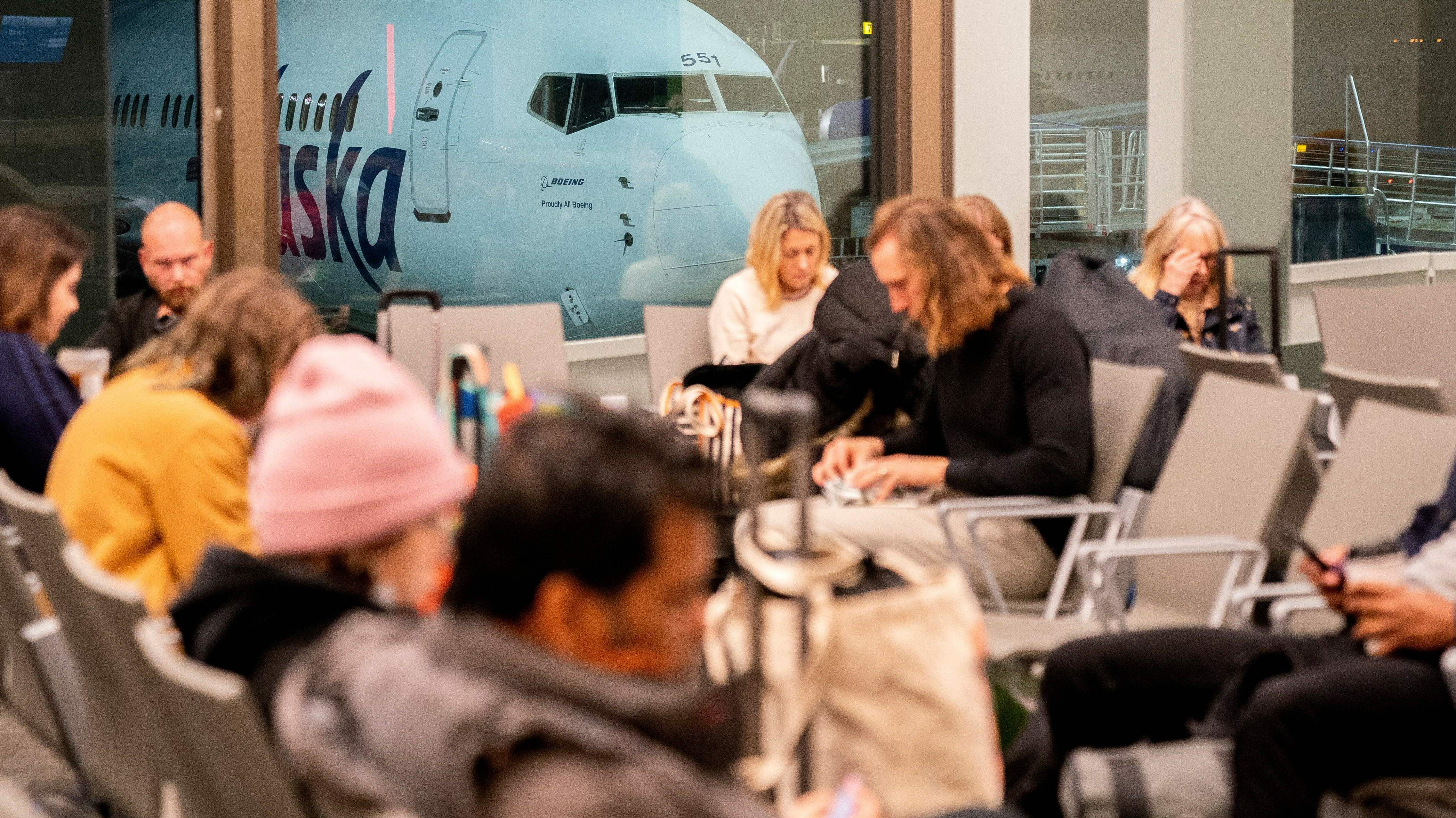 Travelers wait in the terminal as an Alaska Airlines plane sits at a gate at Los Angeles International Airport early Wednesday.