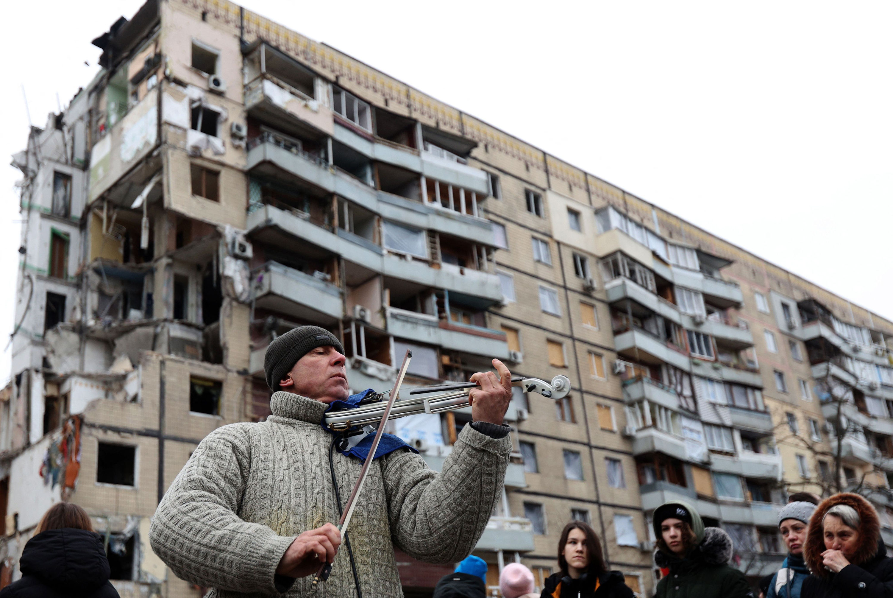 A man plays violin on the sidelines of a religious service held by local residents in front of an apartment building in the Ukrainian city of Dnipro on Sunday. The building was destroyed by a Russian missile strike on Jan. 14. (AFP via Getty Images)