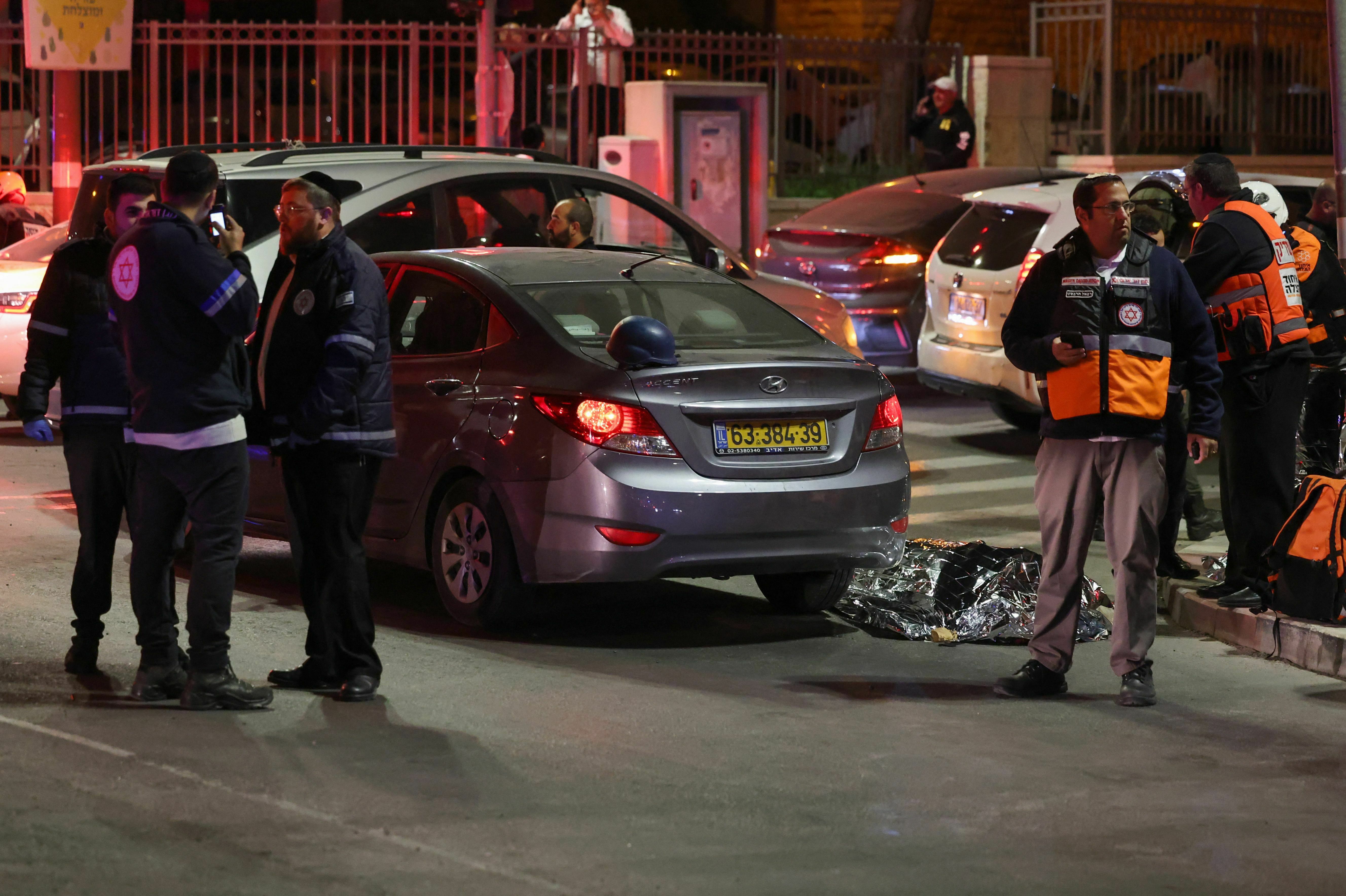 Israeli emergency service personnel and security forces stand near a covered body at the site of a reported attack in Jerusalem on Friday. (AFP via Getty Images)