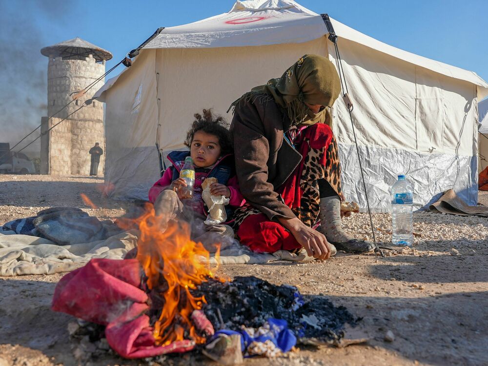 Syrians warm up by a fire at a make-shift shelter for people who were left homeless, near the rebel-held town of Jindayris on Feb. 8, 2023. (AFP via Getty Images)