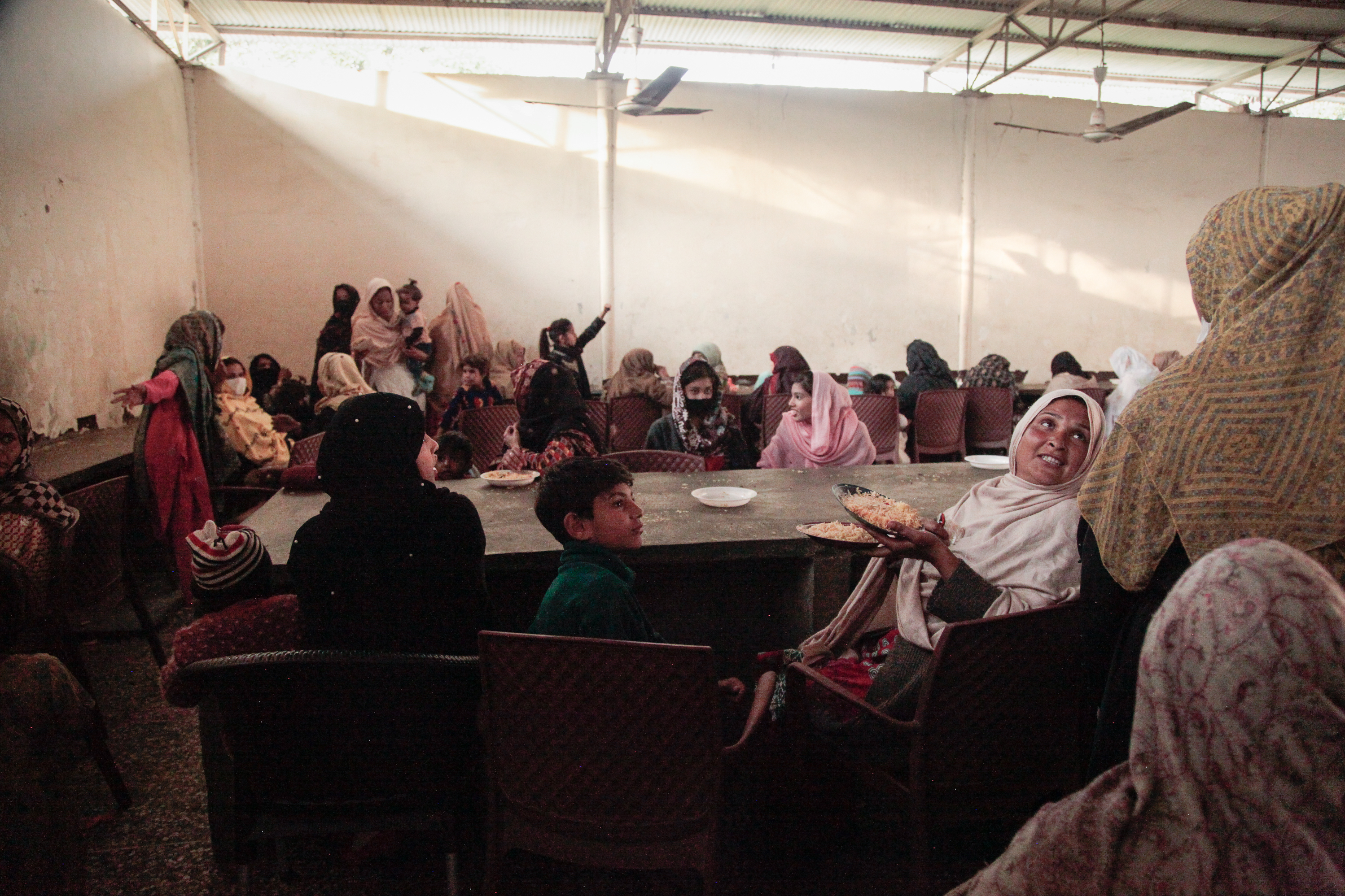 Women sit in a gender-segregated hall, waiting to be served free food cooked in open-air stalls surrounding the shrine to the Sufi saint Bari Imam. Men and women hoping for the saint's blessings pay cooks to prepare the food for hungry shrine visitors.