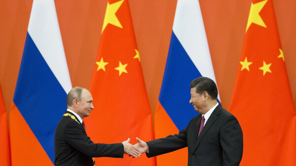 Chinese President Xi Jinping, right, and Russian President Vladimir Putin shake hands in front of giant flags in 2018.
