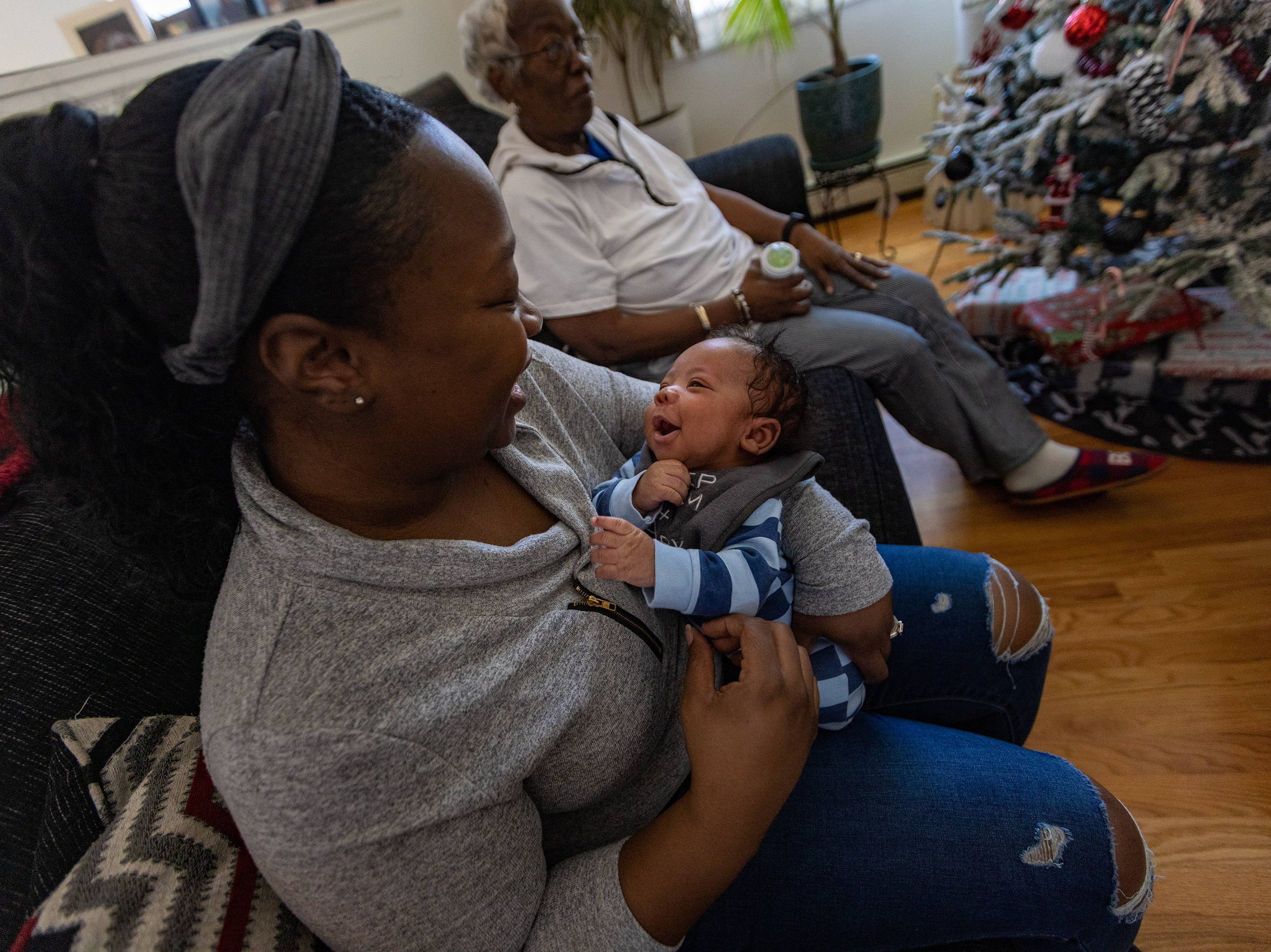 Kennise Nevers holds her son, AJ, in her arms at home. Nevers' mother, Nancy Josey, looks on. (WBUR)