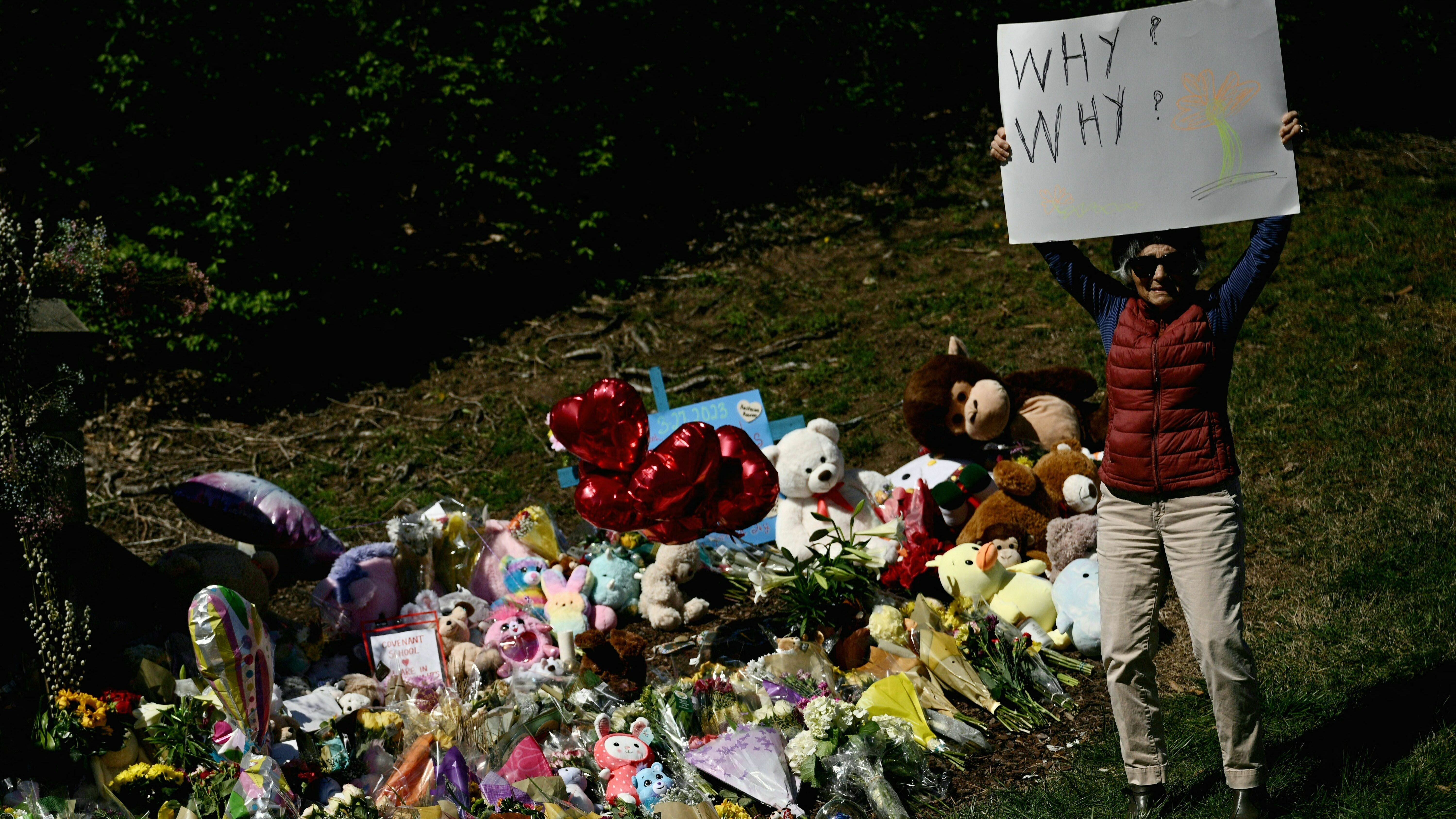 A mourner holds a sign on Wednesday reading "Why? Why?" at a makeshift memorial for victims of a shooting at the Covenant School campus, in Nashville, Tenn.