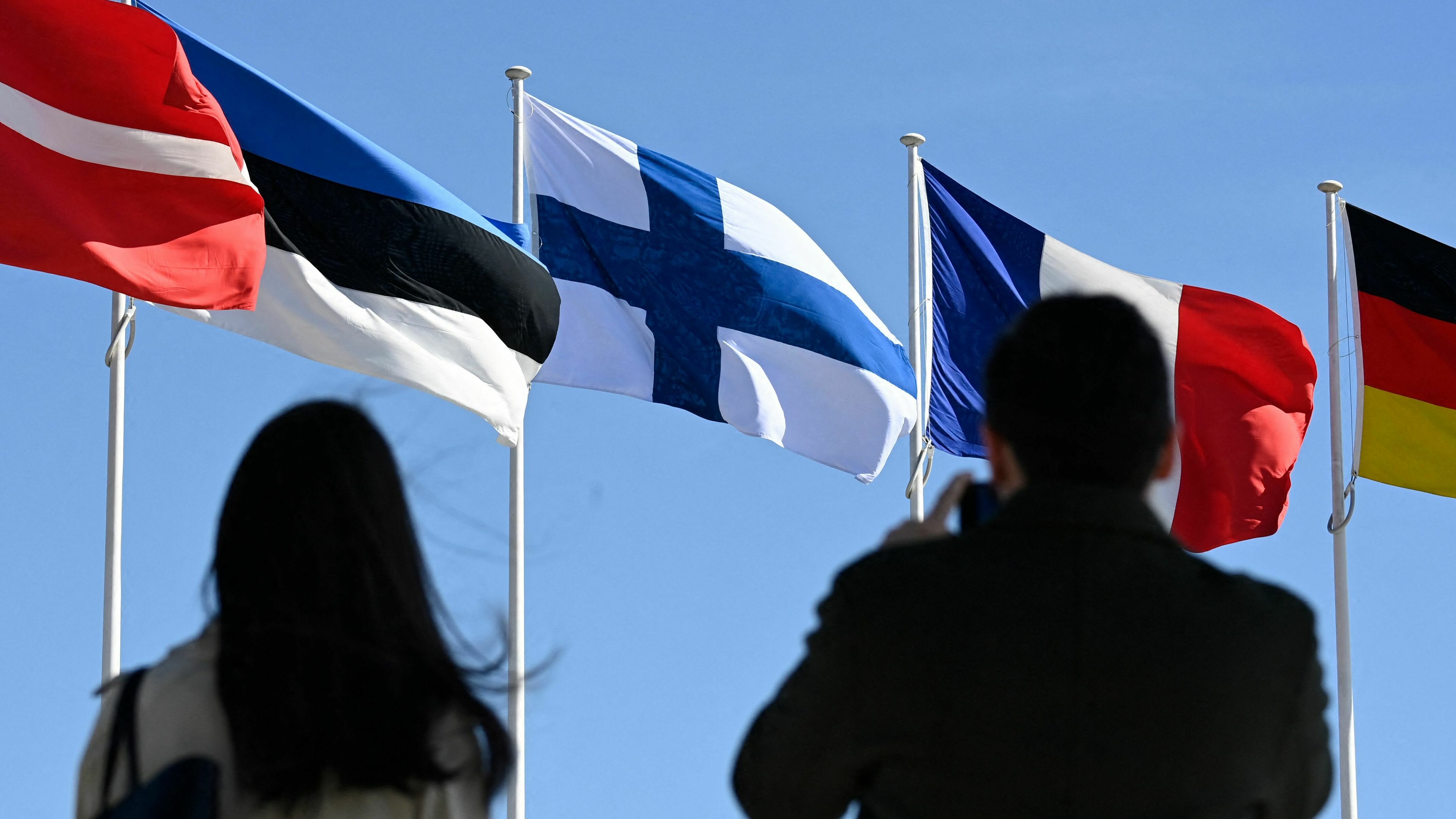 People stand in front of the Finnish national flag after a flag-raising ceremony at the NATO headquarters in Brussels on April 4, 2023. (POOL/AFP via Getty Images)