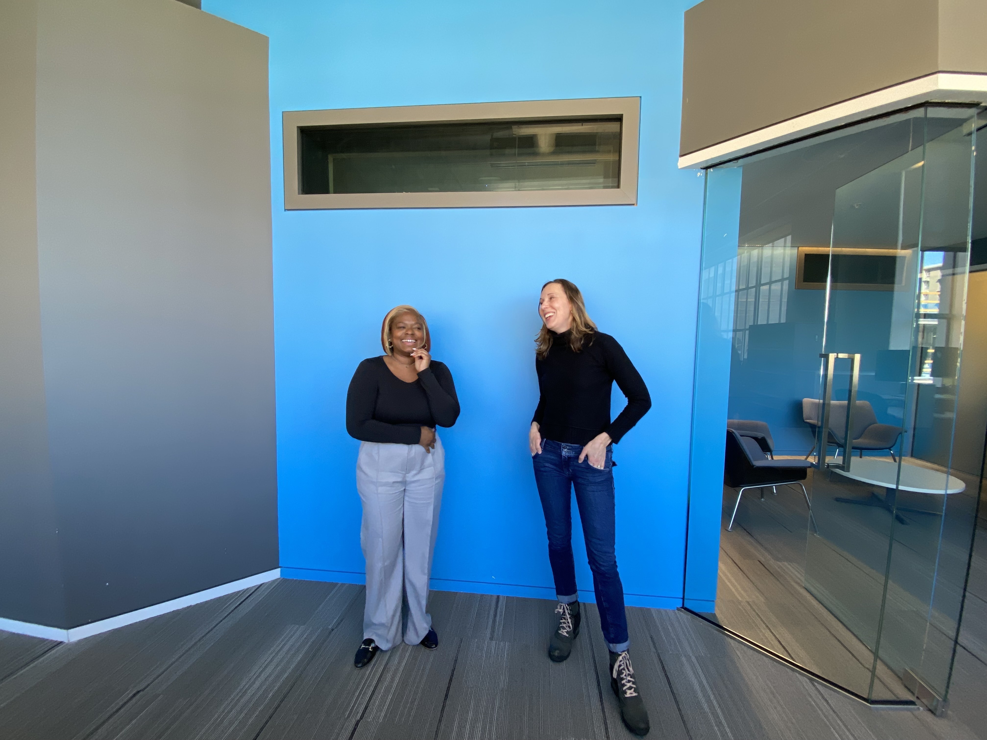 Kelley Dickens (Supervising Editor, Morning Edition) and Miranda Kennedy pose for a photo in front of the blue wall.