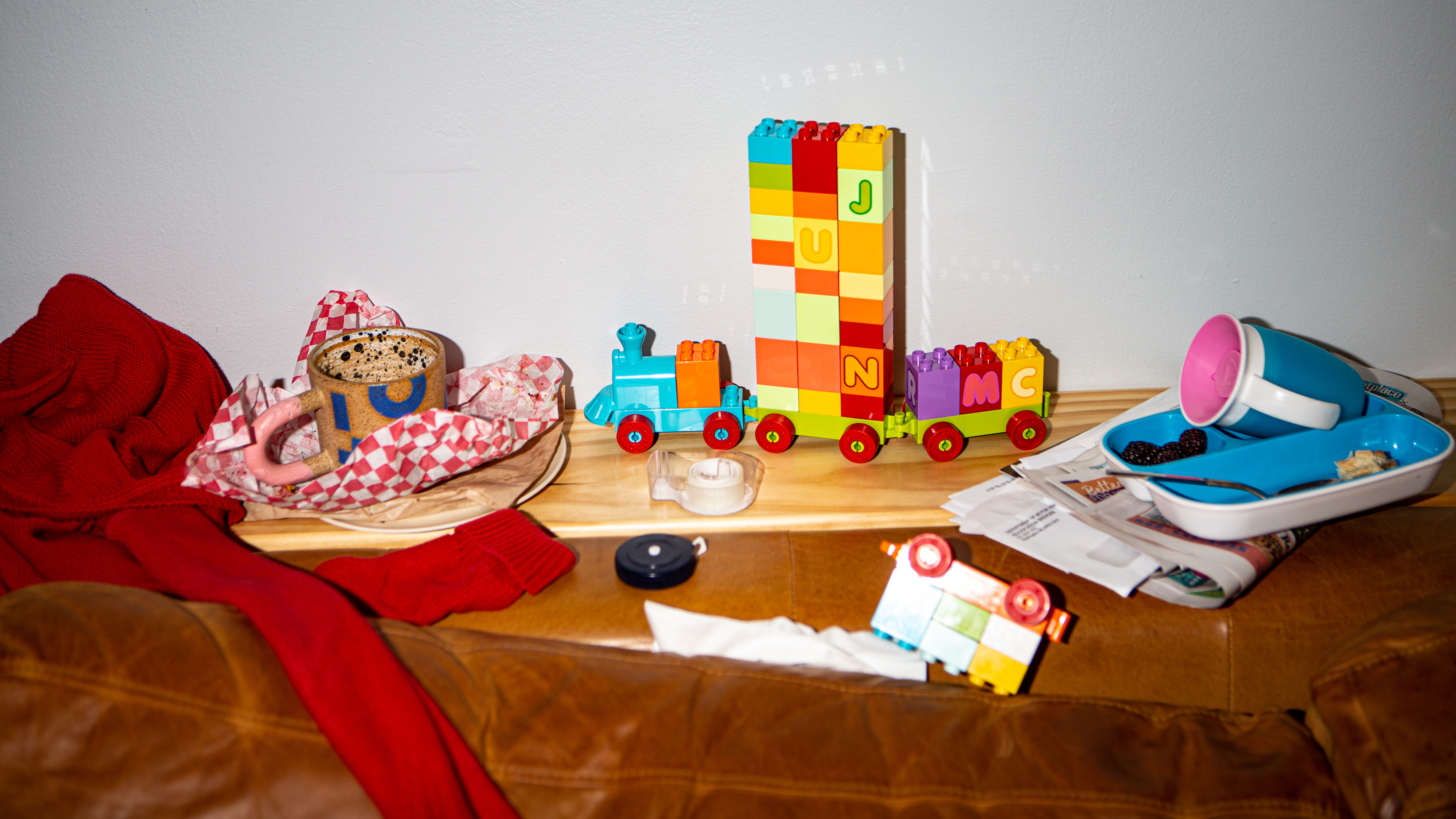 A floor filled with clutter with items such as a toy train, tape, clothes and a newspaper.