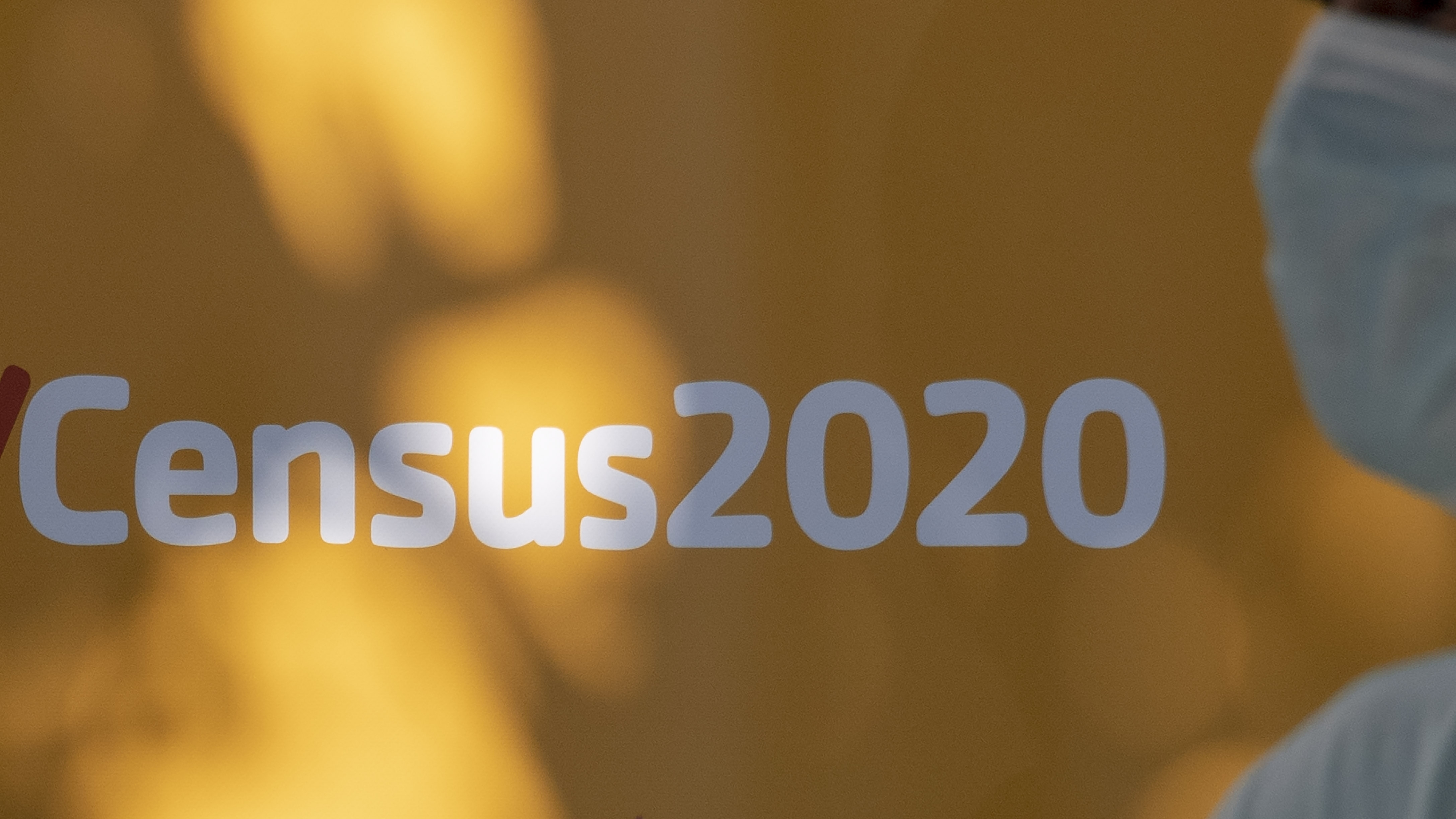 A person wearing a mask walks past a sign encouraging people to complete the 2020 census in Los Angeles.