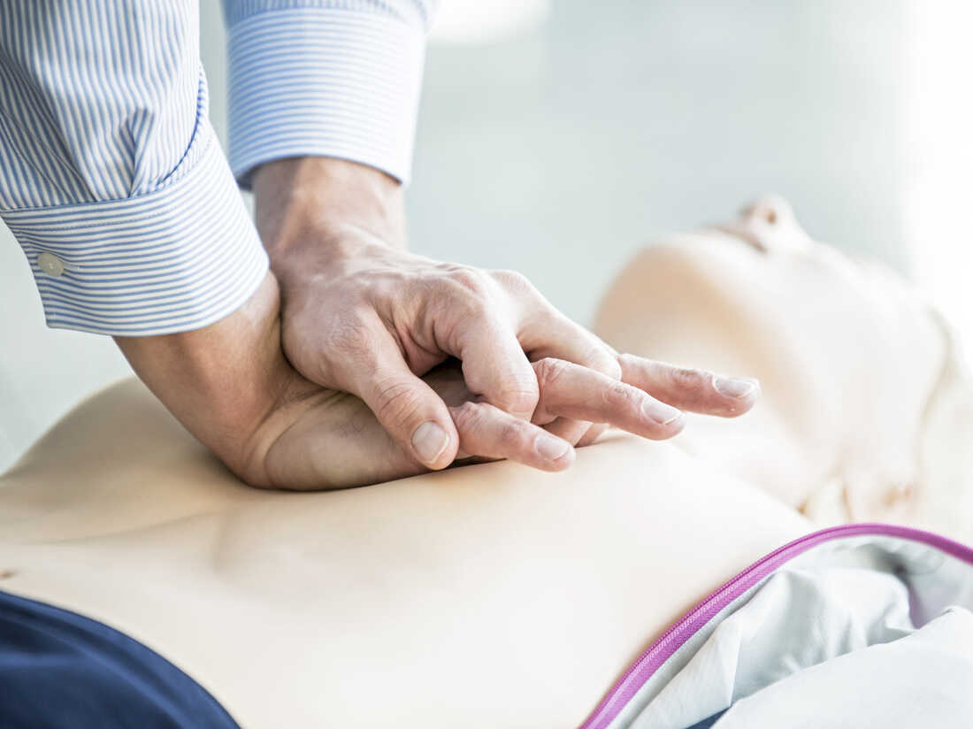 First-aider practising chest compressions on a CPR training dummy.