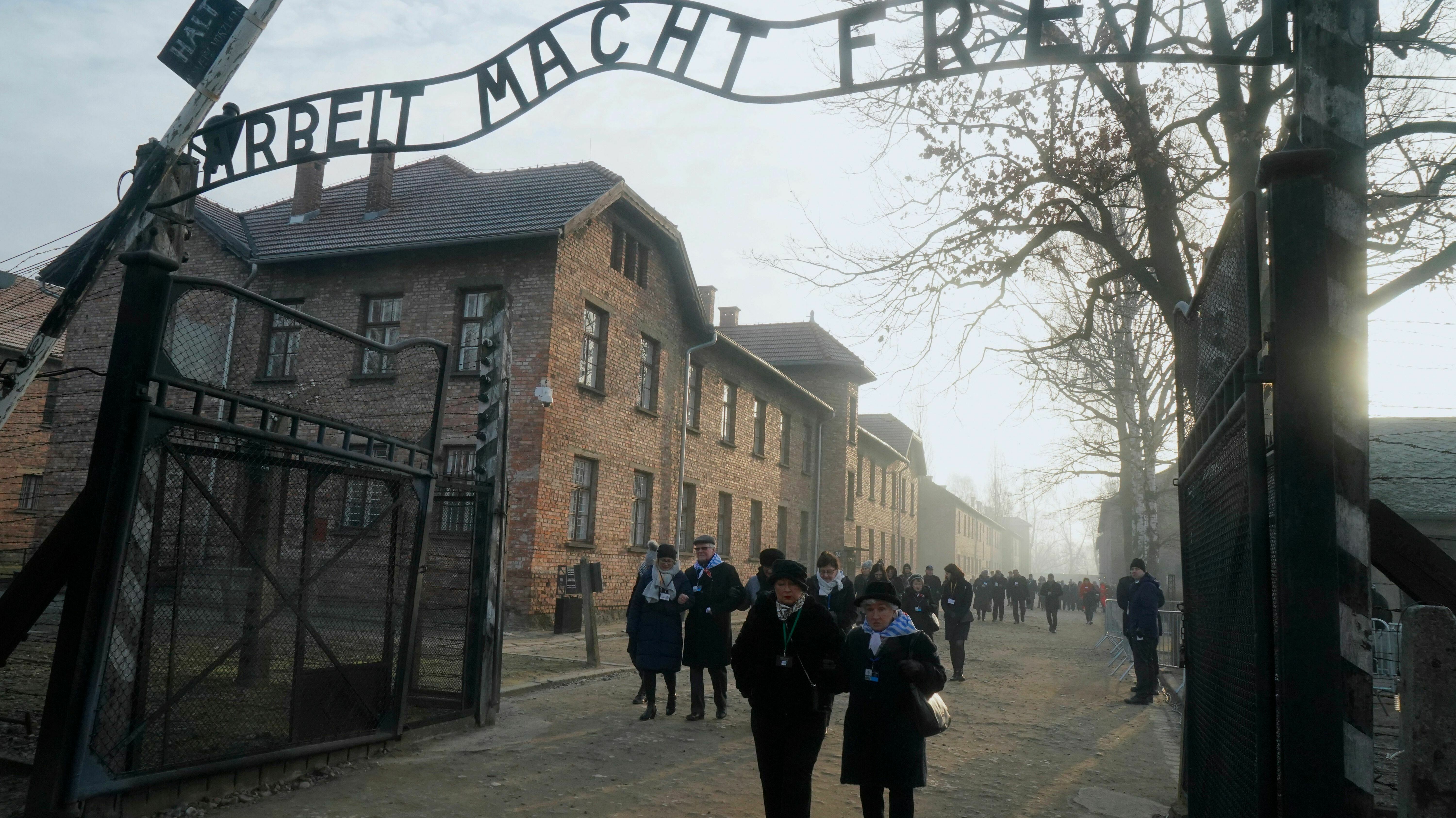 In this 2020 photo, survivors walk below a gate with the inscription "Work sets you free" after a wreath-laying ceremony at the memorial site of the former German Nazi death camp Auschwitz during ceremonies marking the 75th anniversary of the camp