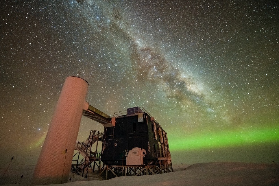 The IceCube Lab under a starry, night sky, with the Milky Way appearing over low auroras in the background. (Yuya Makino, IceCube/NSF)