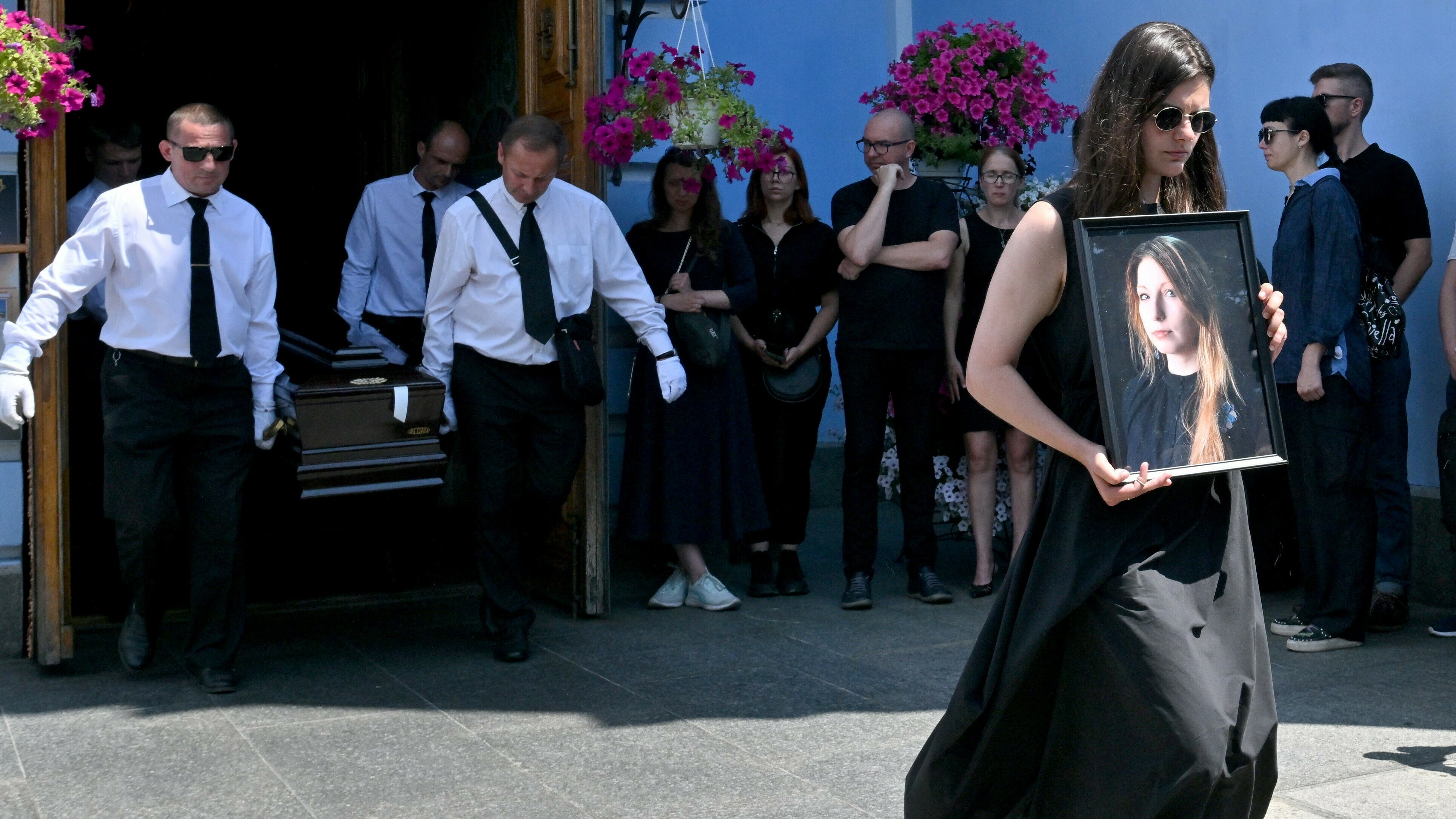 A woman holds a picture of Victoria Amelina, as pallbearers carry the writer