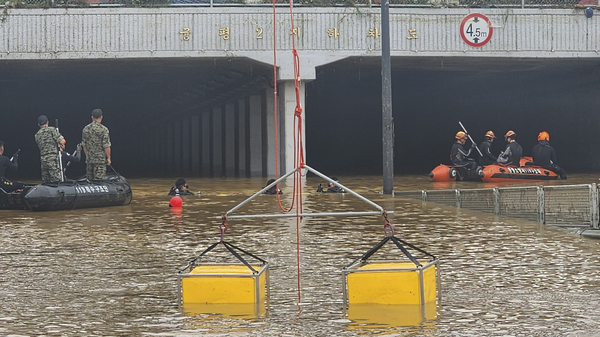 In this photo provided by South Korea National Fire Agency, rescuers search along a road submerged by floodwaters leading to an underground tunnel in Cheongju, South Korea,  on Sunday.